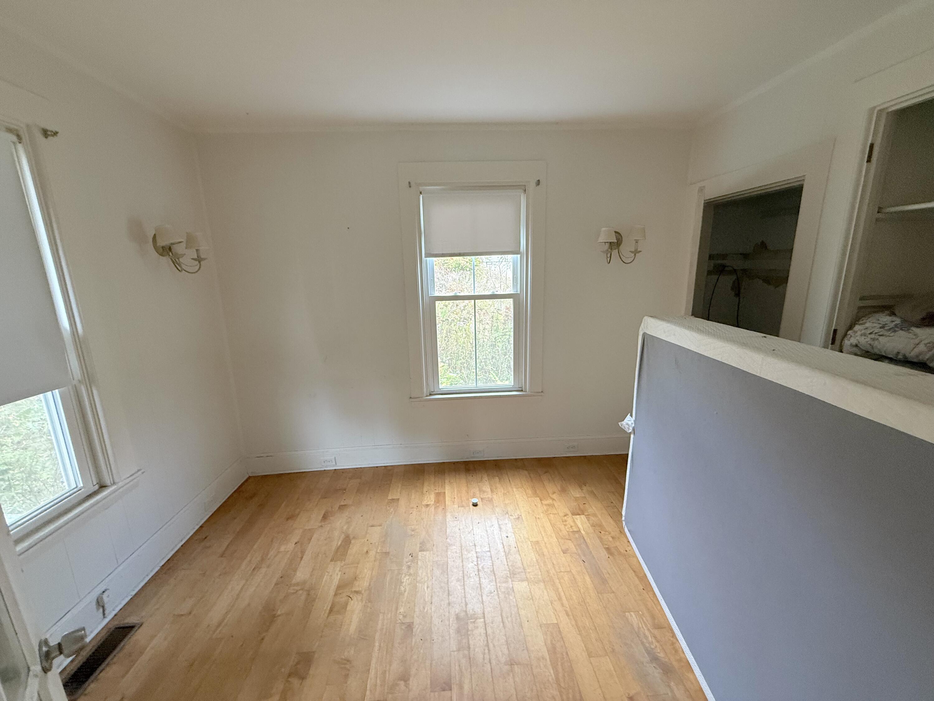 Vacant bedroom with hardwood floors, shaded windows, wall sconces, and a half-height partition.