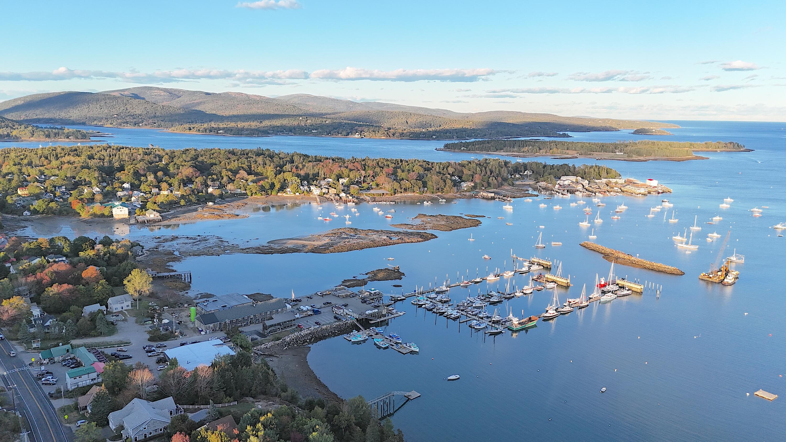 Aerial view of Southwest Harbor harbor, marina, wooded islands, and autumn-colored hills.