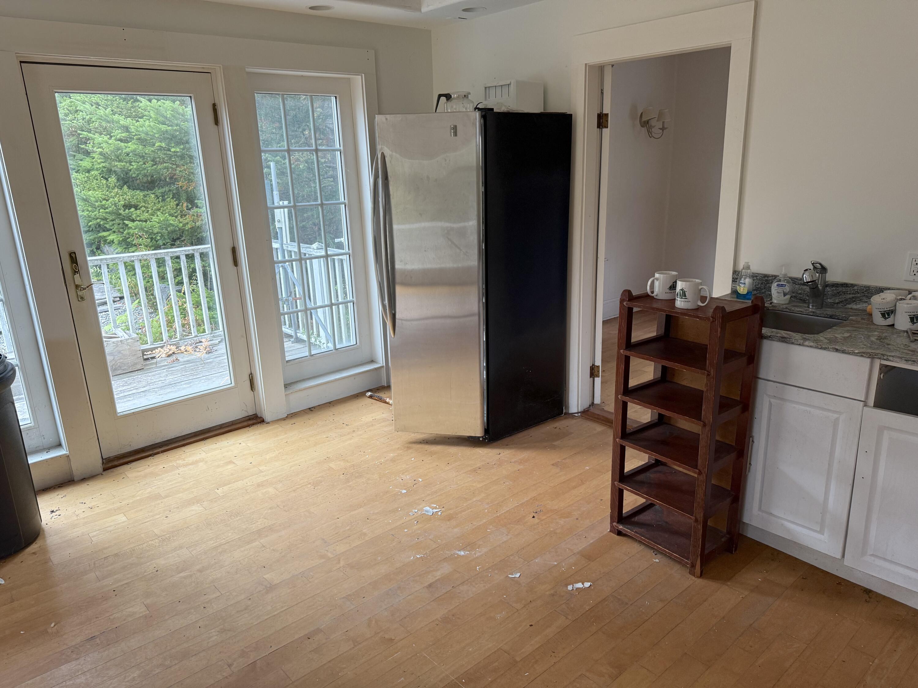 Mostly empty kitchen with a stainless-steel refrigerator and glass doors opening onto a tree-lined deck.