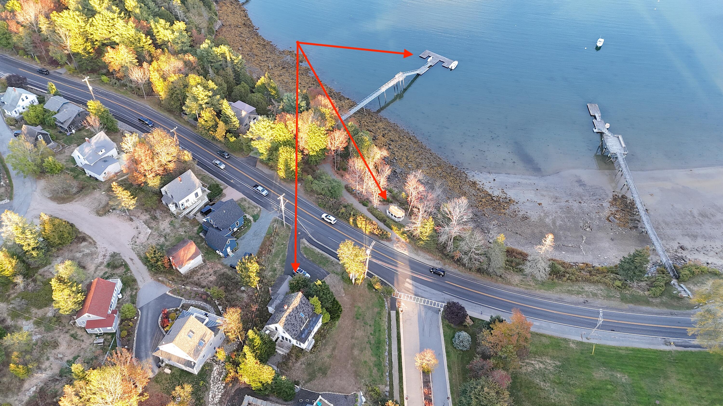 Aerial view of a waterfront property marked by red arrows, with a dock extending into the water.