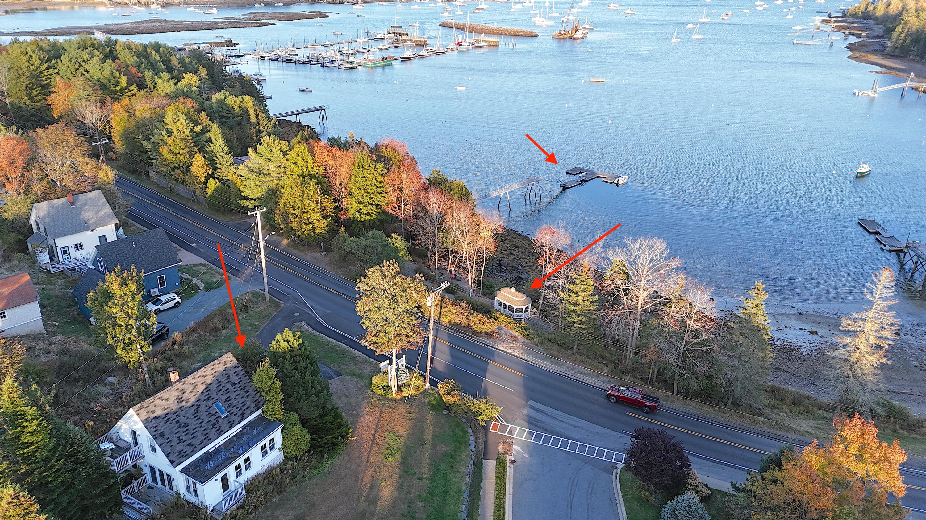 Aerial view of a waterfront house, shore-side structure, and dock marked by red arrows beside a boat-filled harbor.