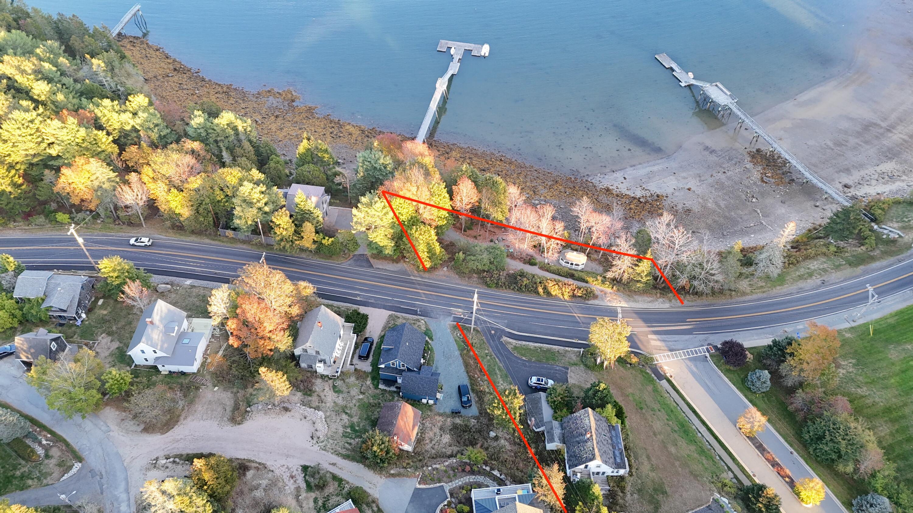 Aerial view of coastal land outlined in red beside a road, rocky shoreline, and docks.