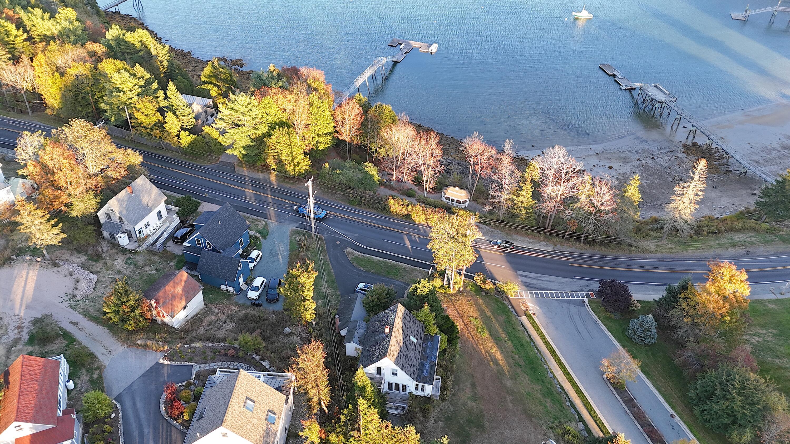 Aerial view of coastal homes beside a harbor, with docks and autumn foliage.
