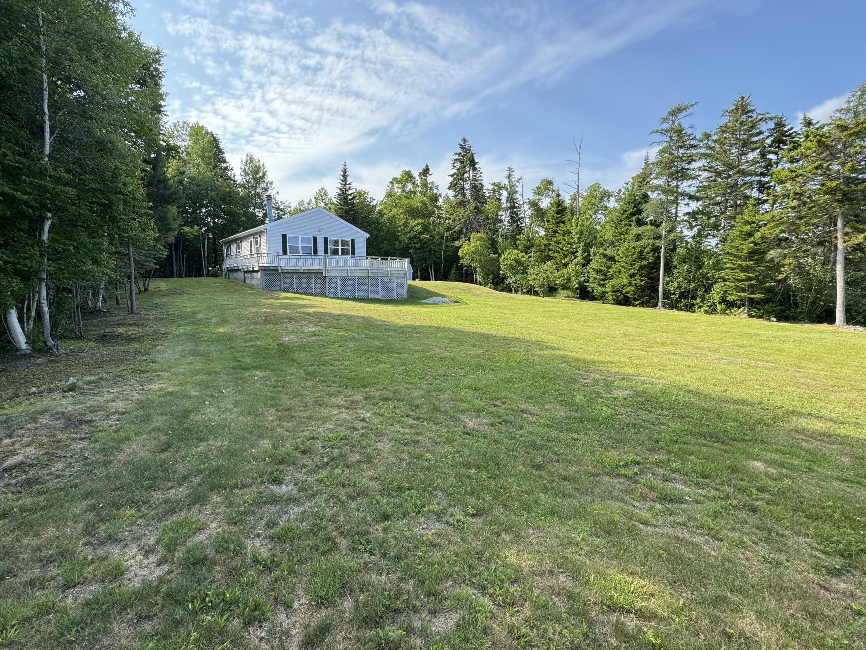 House with a raised deck beyond a broad lawn, surrounded by trees.
