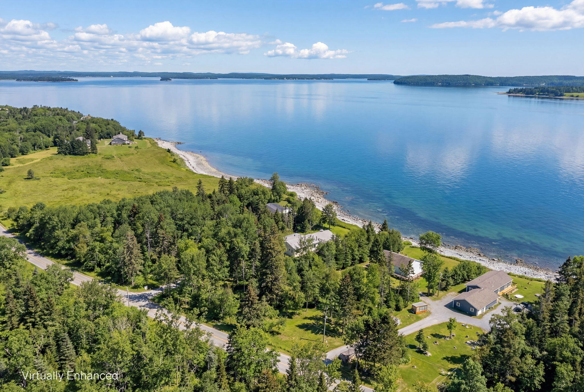 Aerial view of homes along a wooded rocky shoreline beside broad blue water.