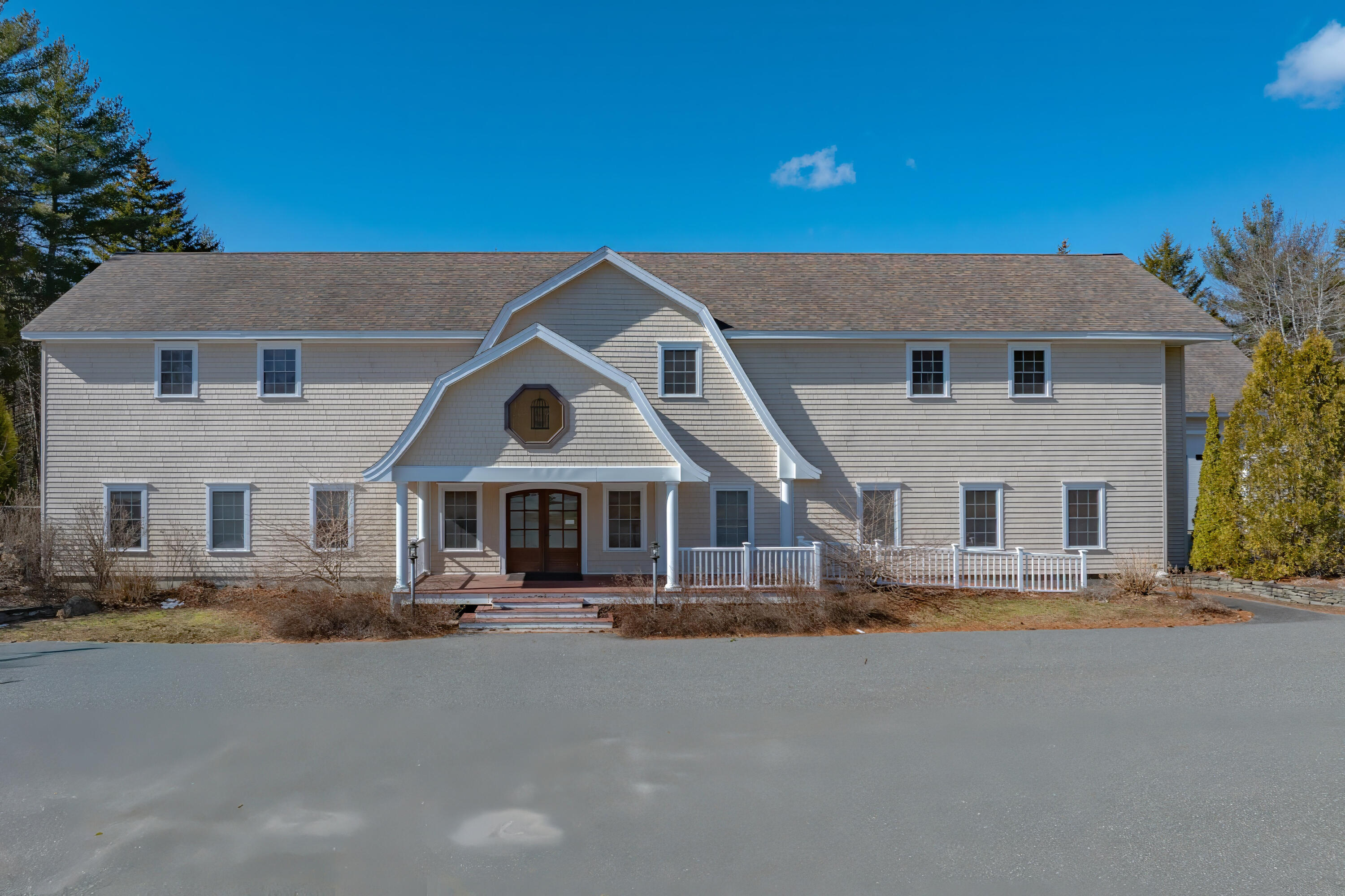 Gray two-story shingle building with a distinctive central gable, octagonal window, and white entrance railings.