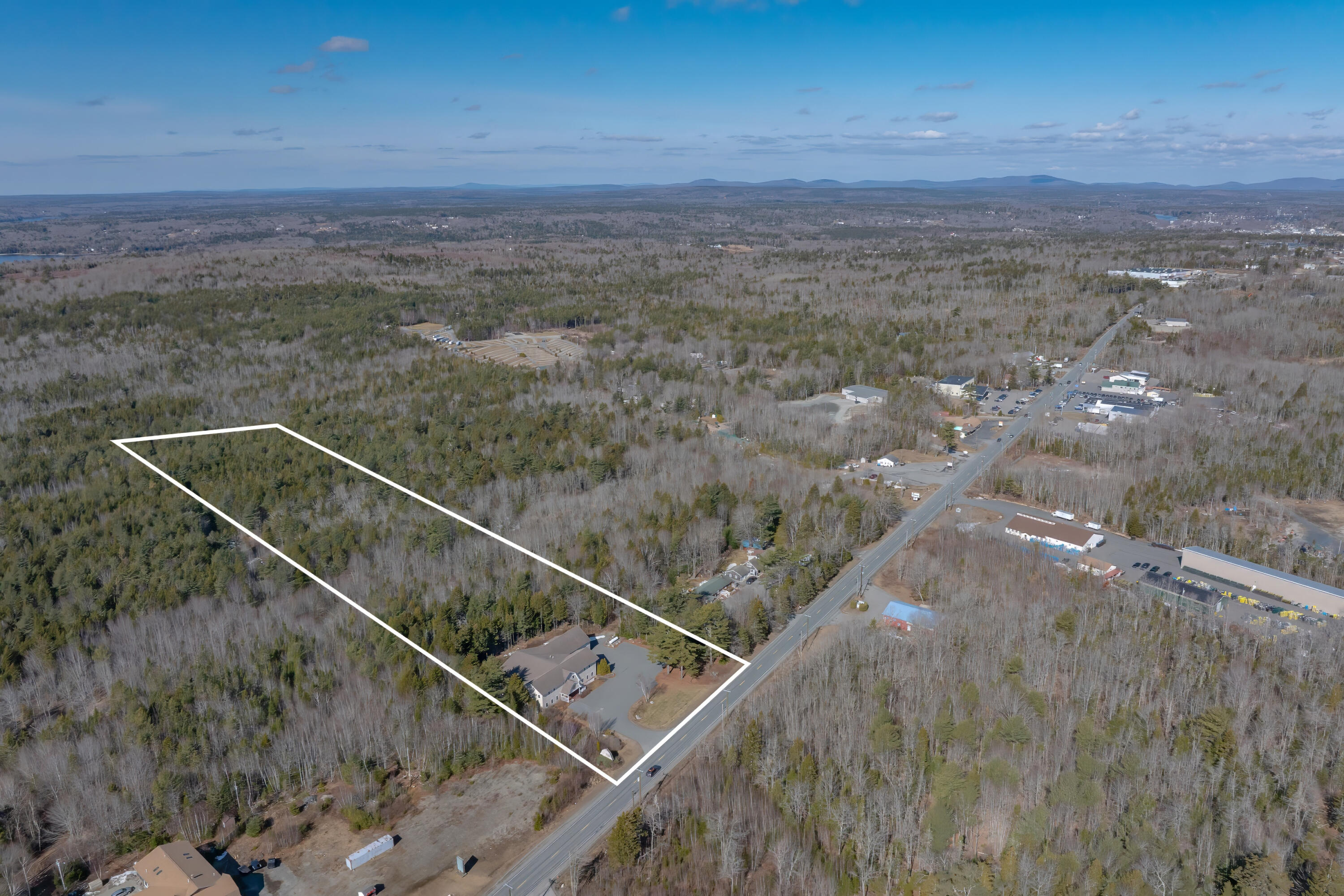 Aerial view of a wooded parcel outlined in white, with a building beside the road.