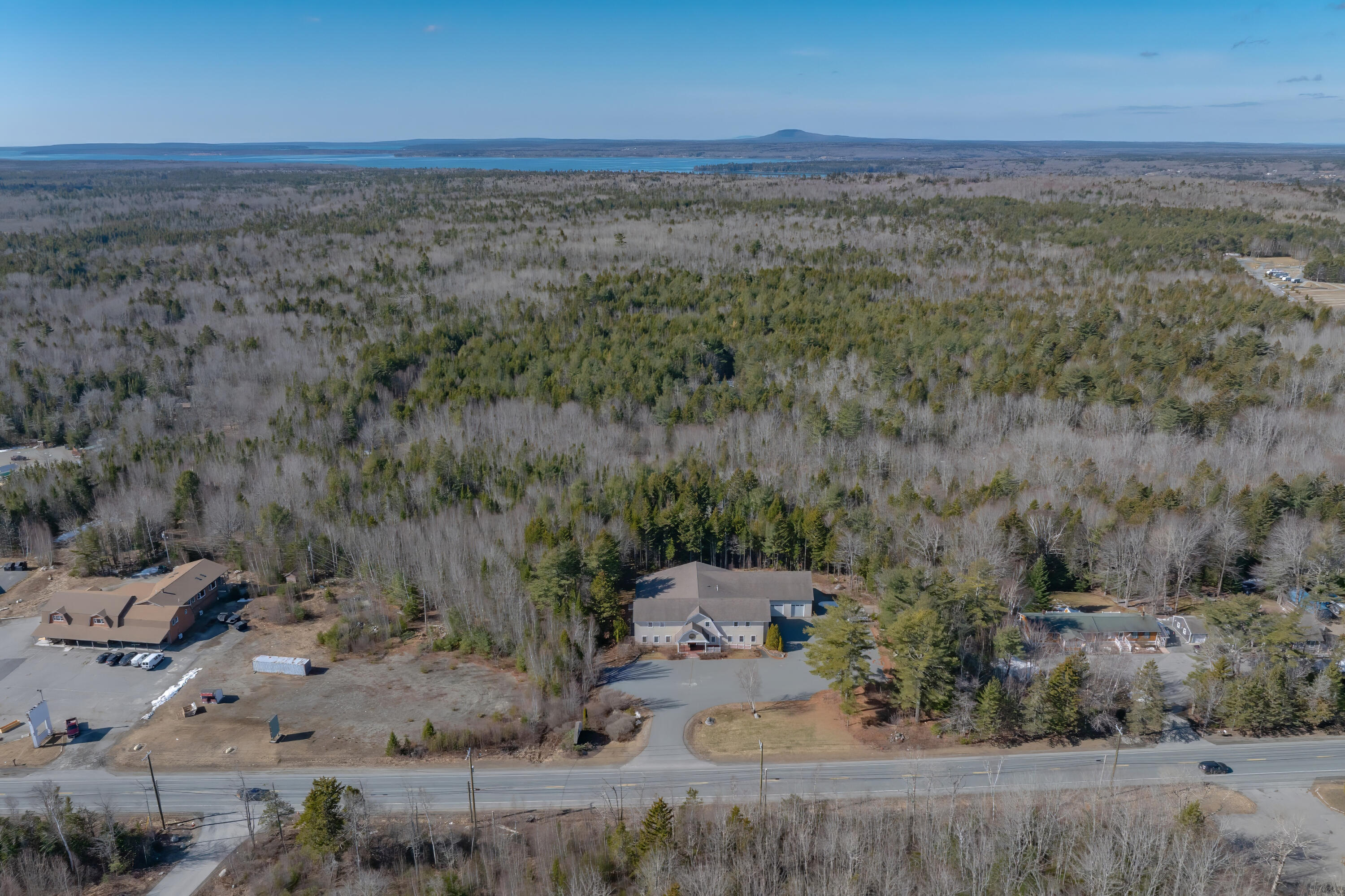 Aerial view of the property and surrounding woods, with distant water beyond the road.