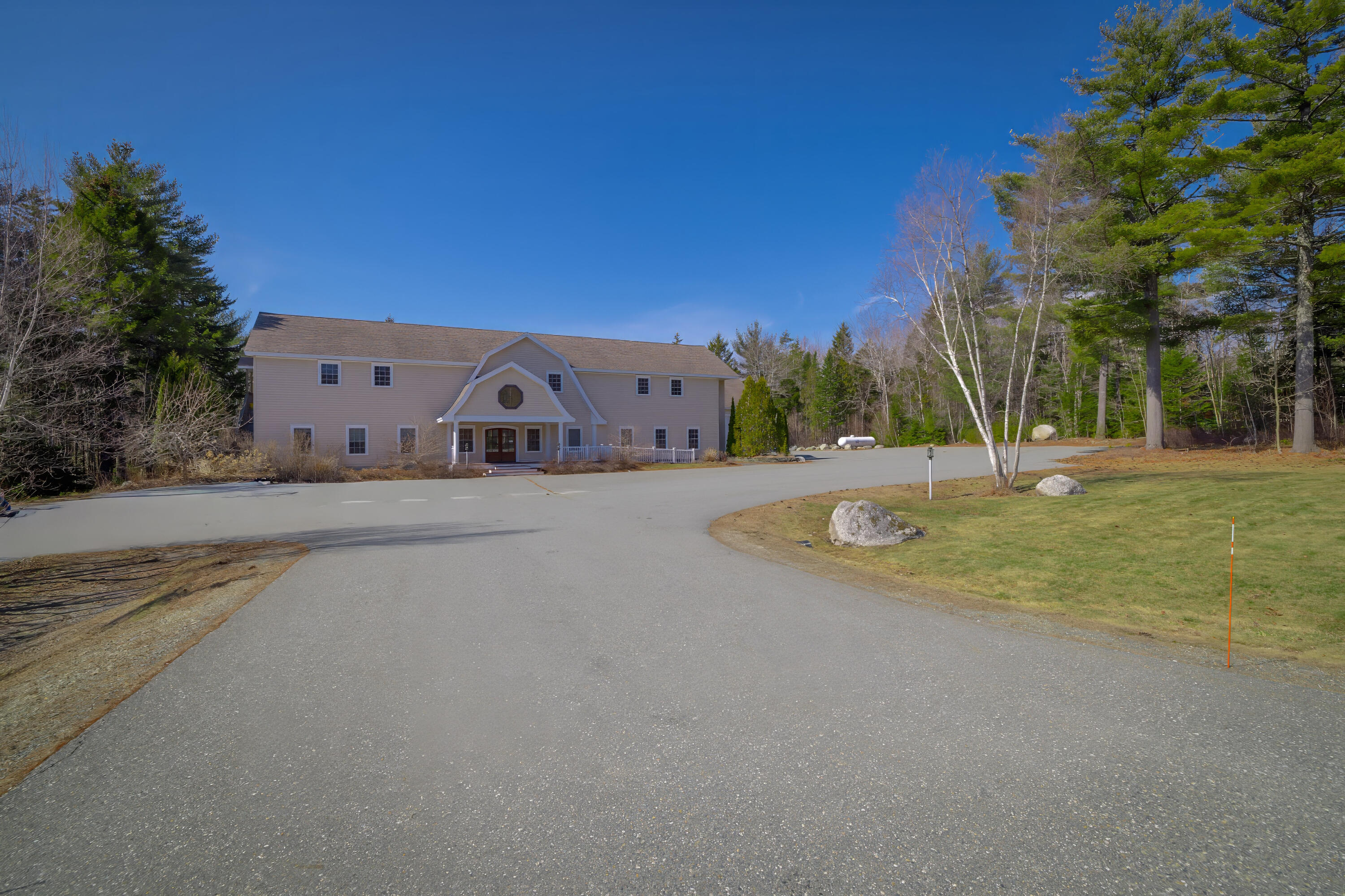Two-story building with a peaked entrance, broad paved driveway, lawn, and surrounding trees.