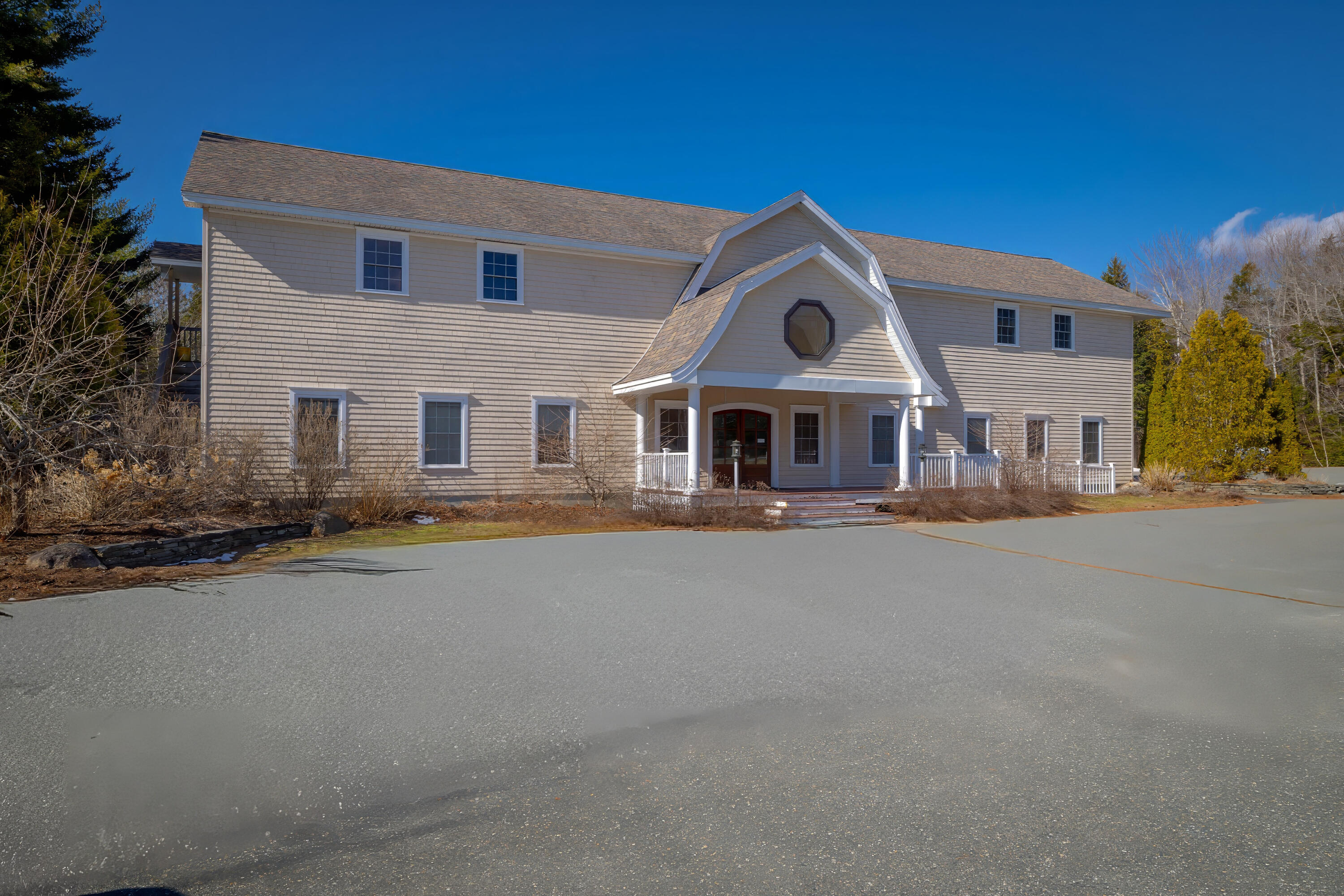 Two-story beige building with a gabled entrance and octagonal window beside a broad paved driveway.