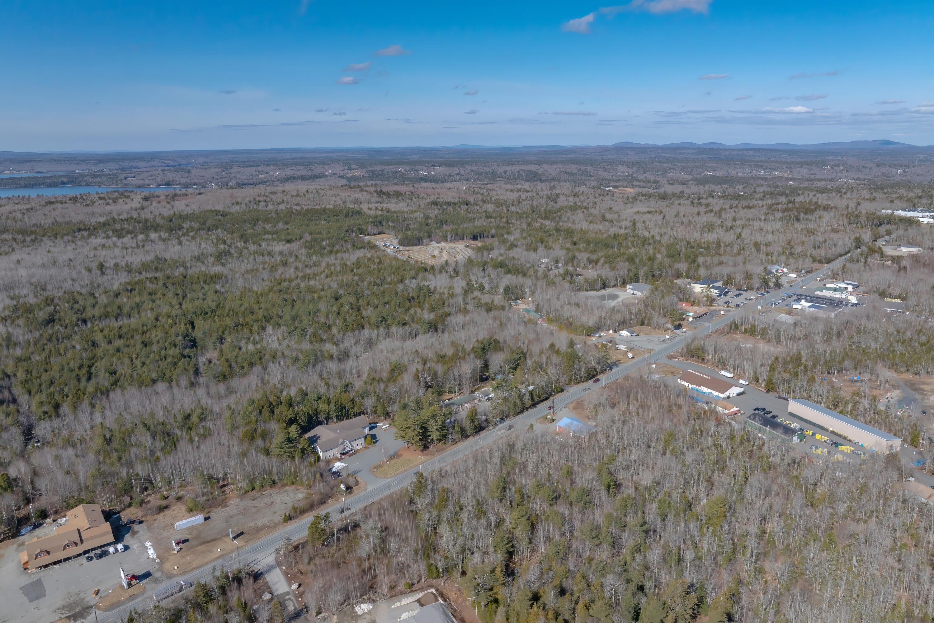 Aerial view of a wooded Trenton landscape, with a road, scattered buildings, distant water, and low mountains.
