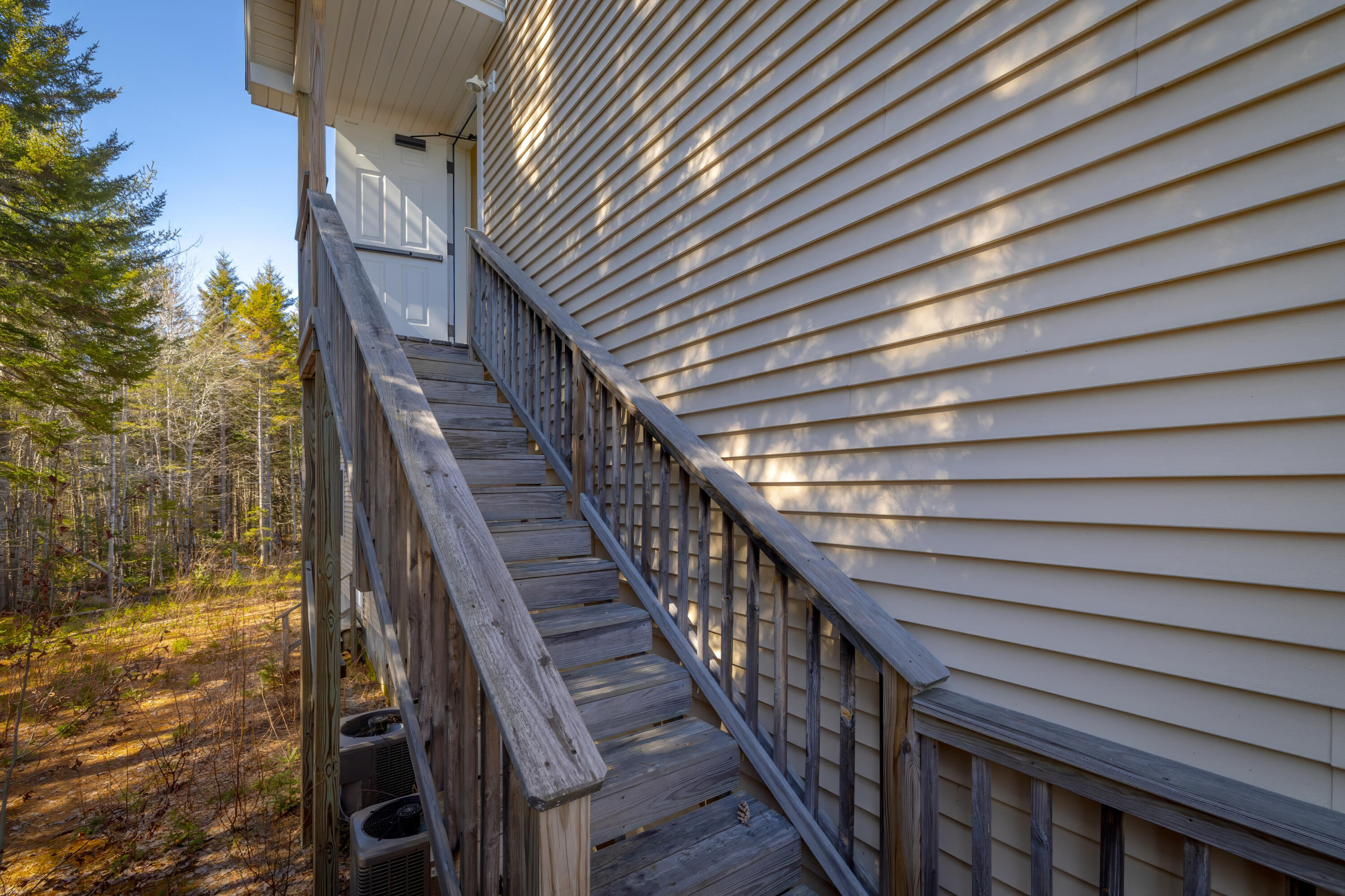 Wooden stairs lead to a white-sided home entrance beside autumn woodland.