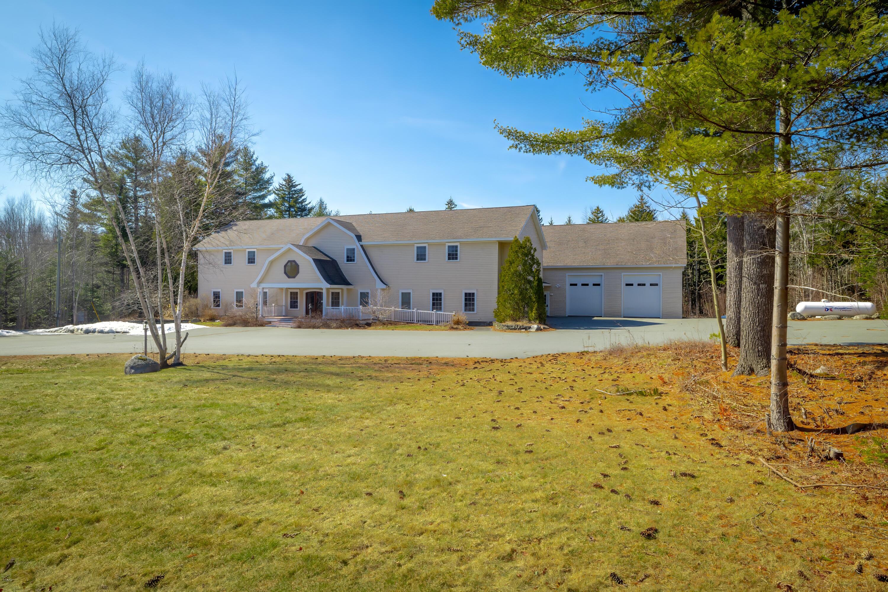 Two-story beige house with a covered porch, attached two-car garage, and broad driveway.