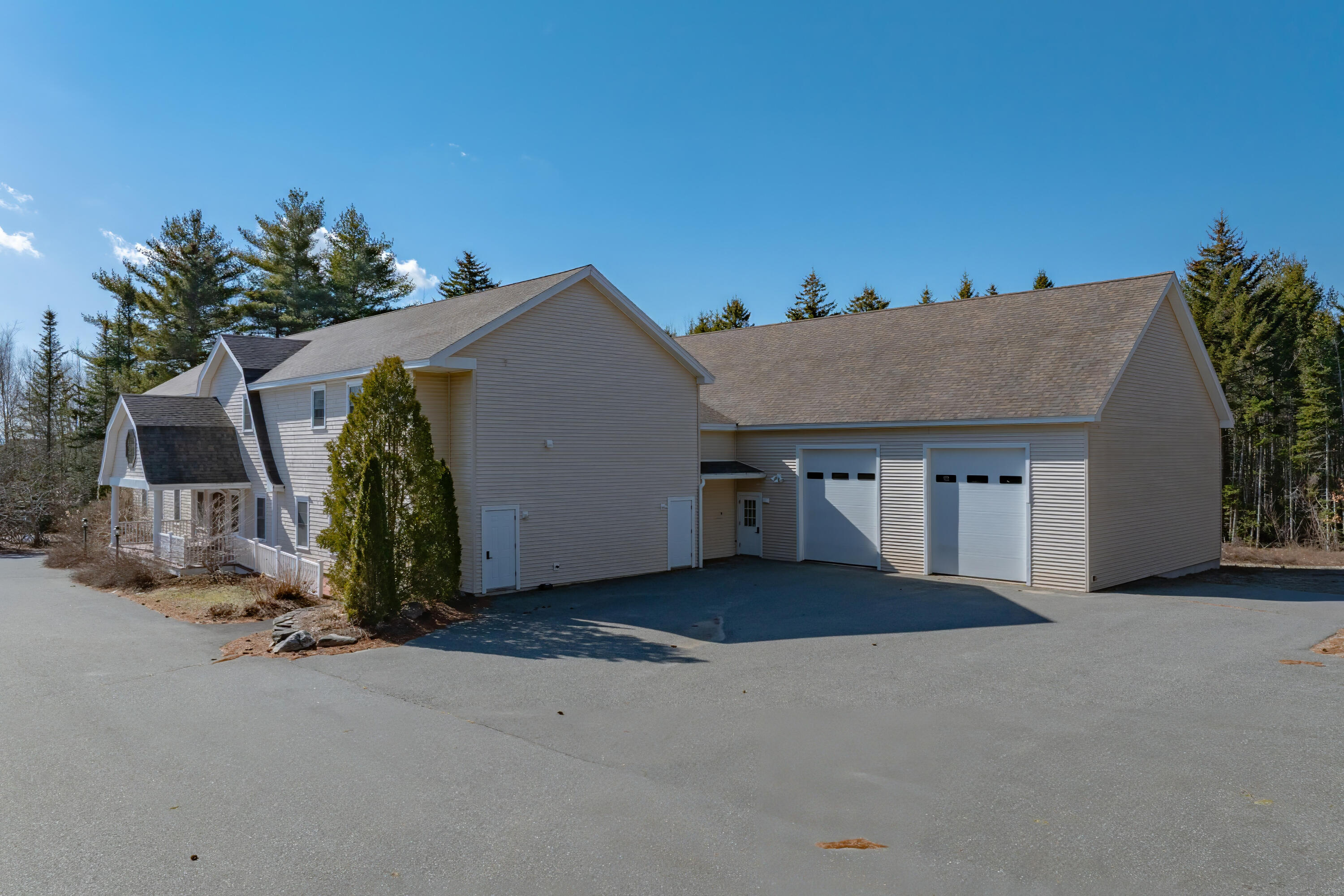 Light-sided home with a covered porch and attached two-bay garage beside a broad paved driveway.