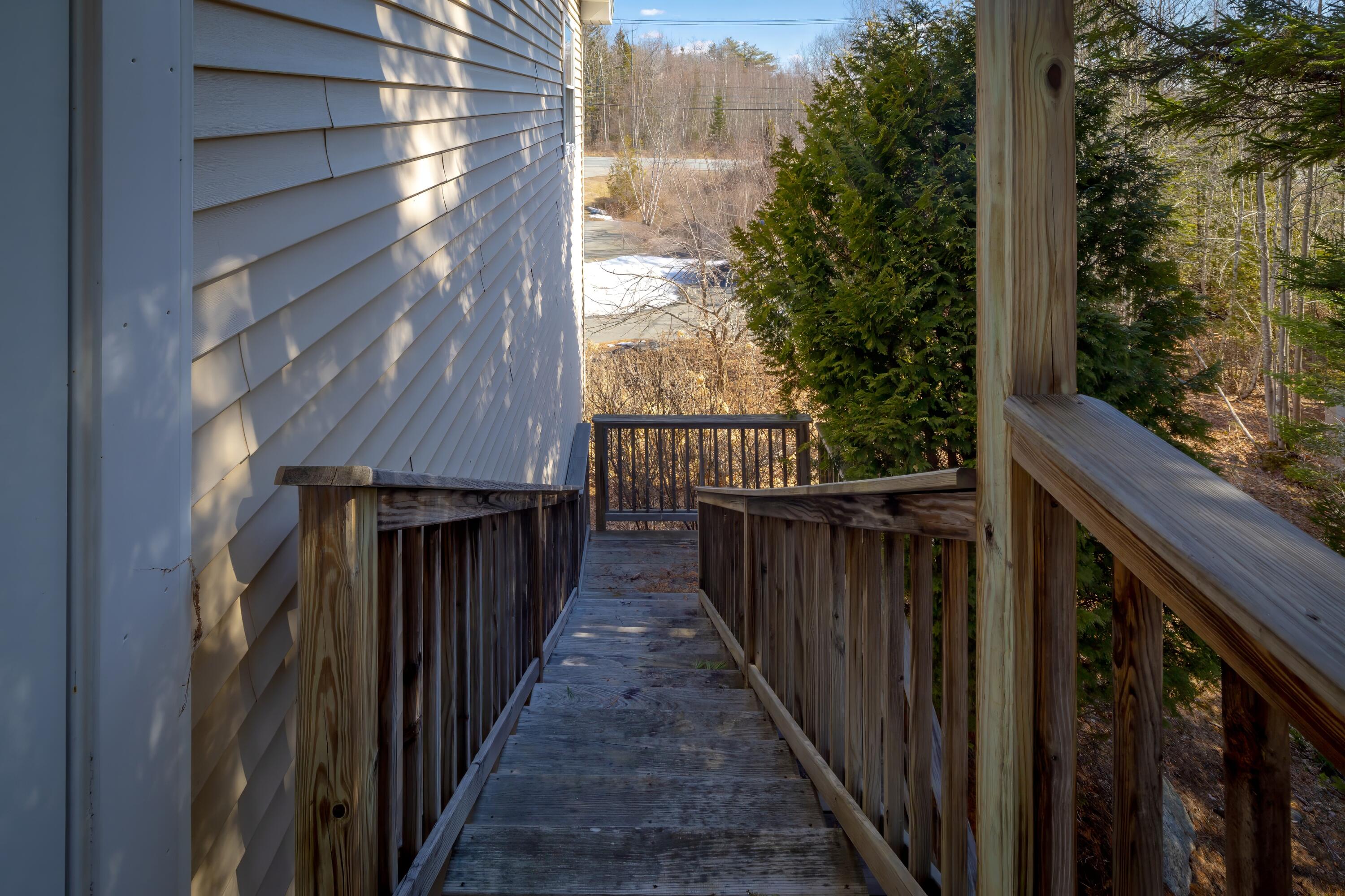 Wooden ramp and railings beside the house, leading toward a wooded yard with patches of snow.
