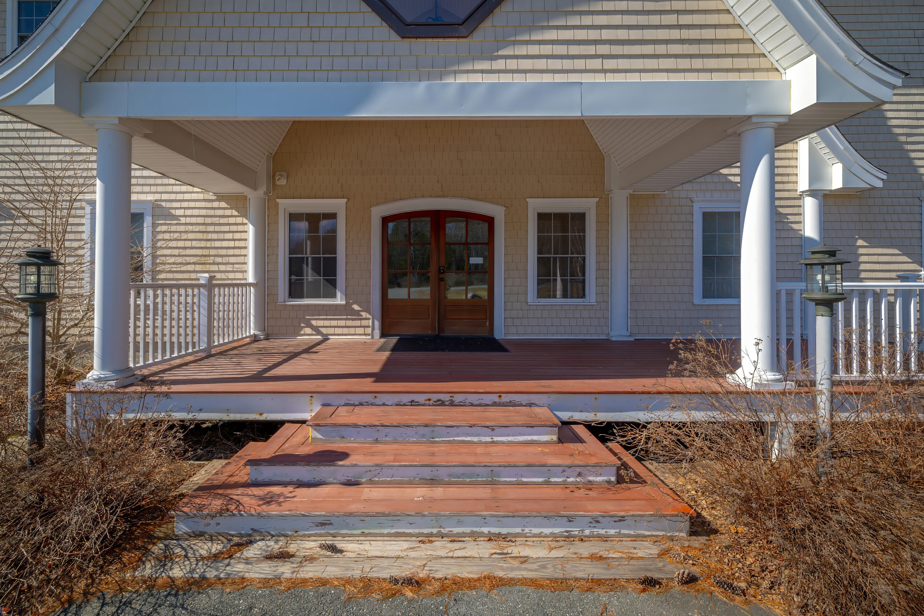 Home’s covered front porch with white columns, double wooden doors, and broad wooden steps.