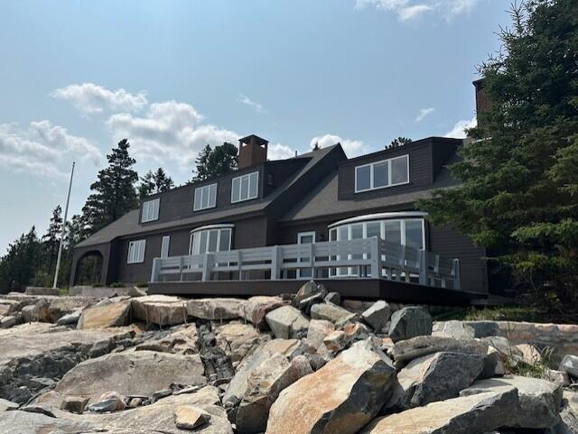 Coastal home with a broad gray deck above a rocky shoreline.