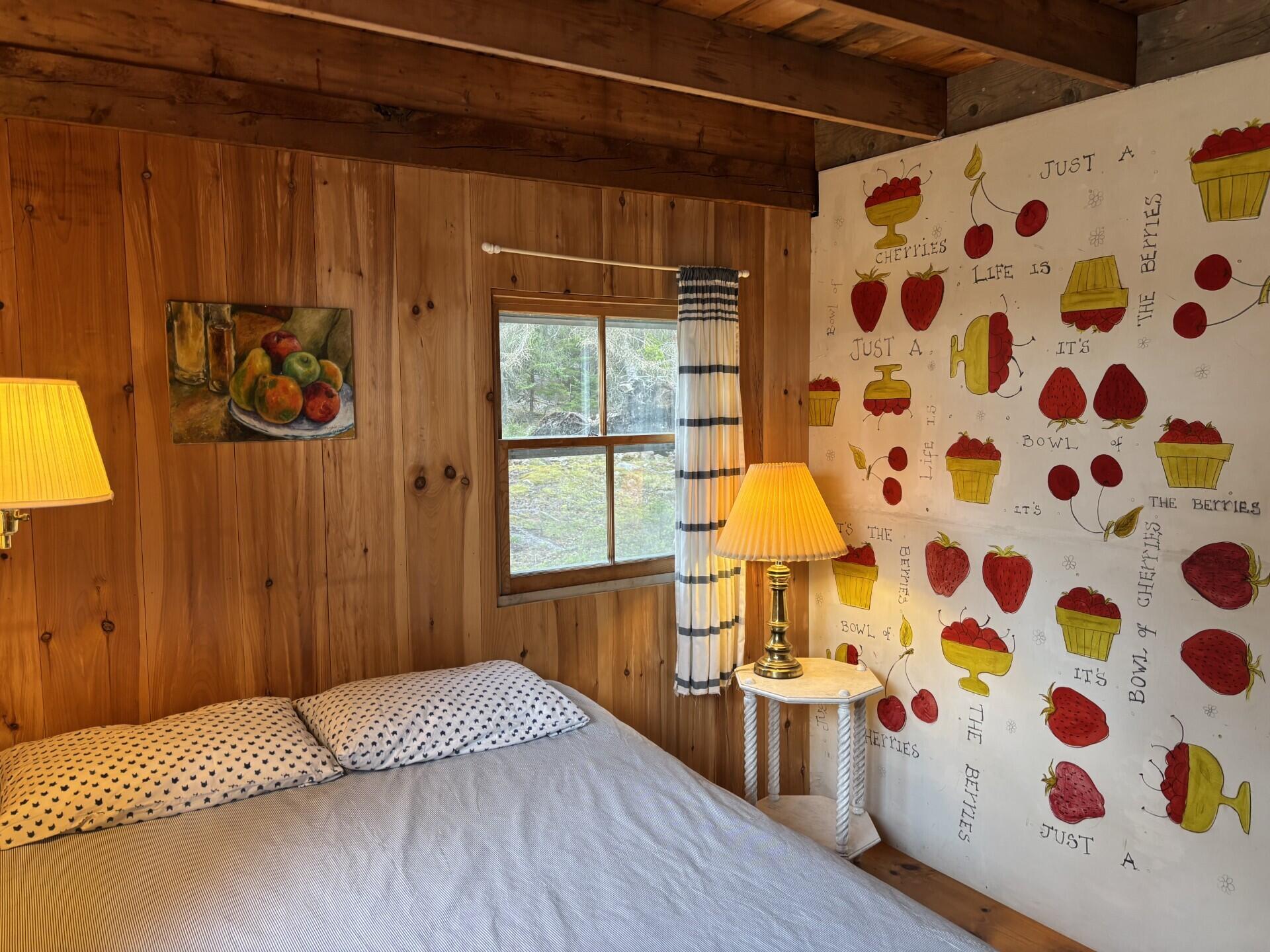 Bedroom with wood-paneled walls, berry-patterned wallpaper, and a window overlooking greenery.