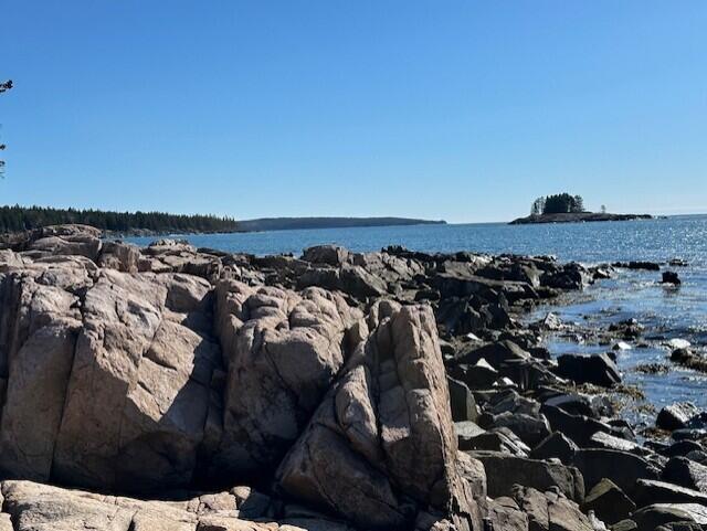 Rocky granite shoreline beside blue ocean, with a small tree-covered island offshore.