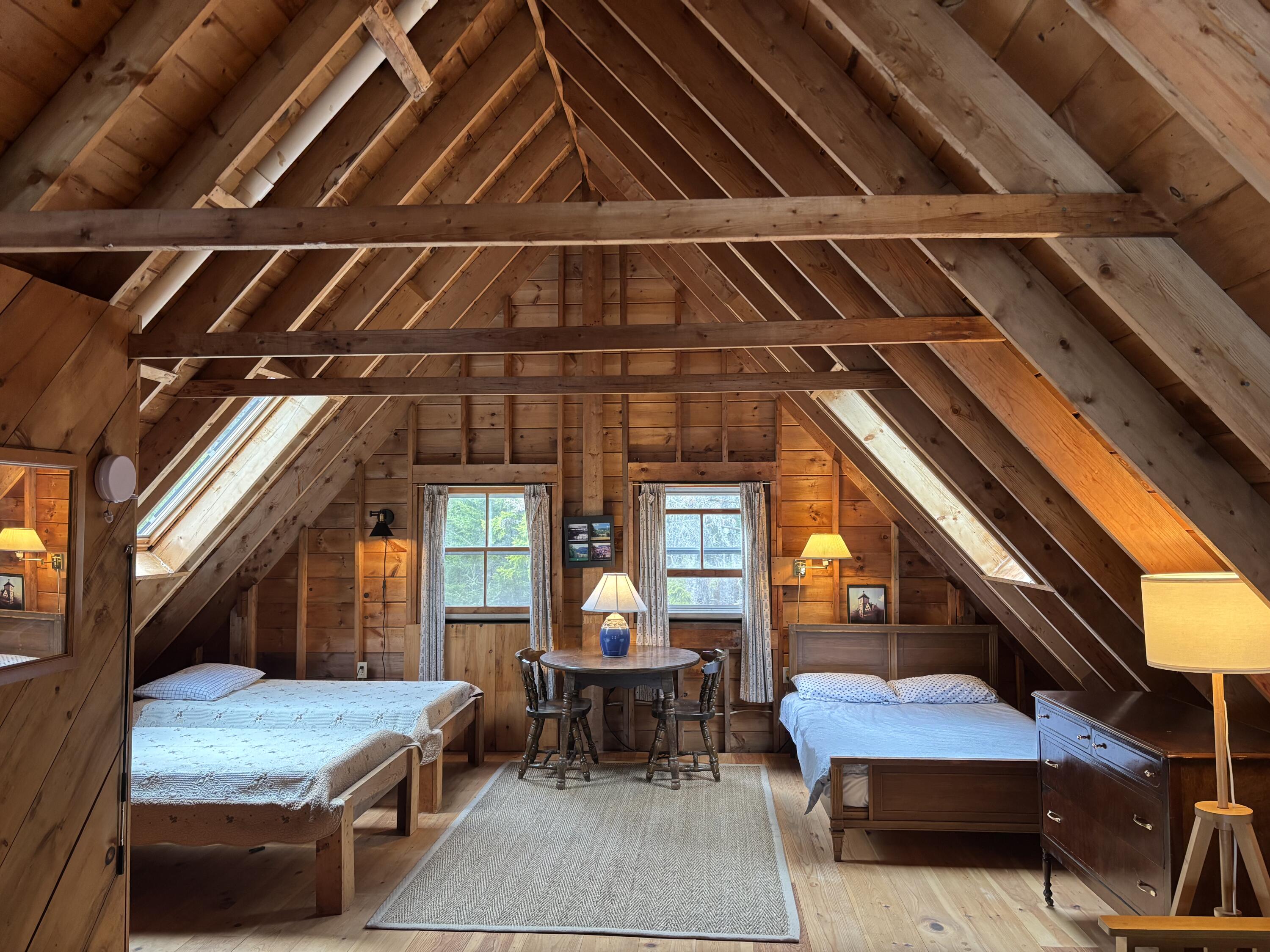 Attic bedroom with two beds, exposed timber beams, skylights, and a small table between the beds.