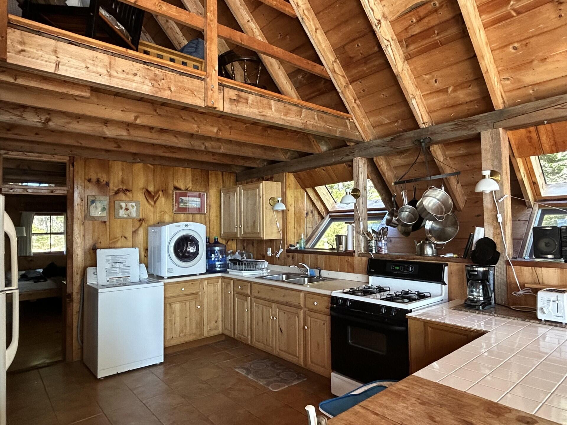 Rustic wood kitchen with exposed rafters, hanging pots, gas range, and laundry machines.