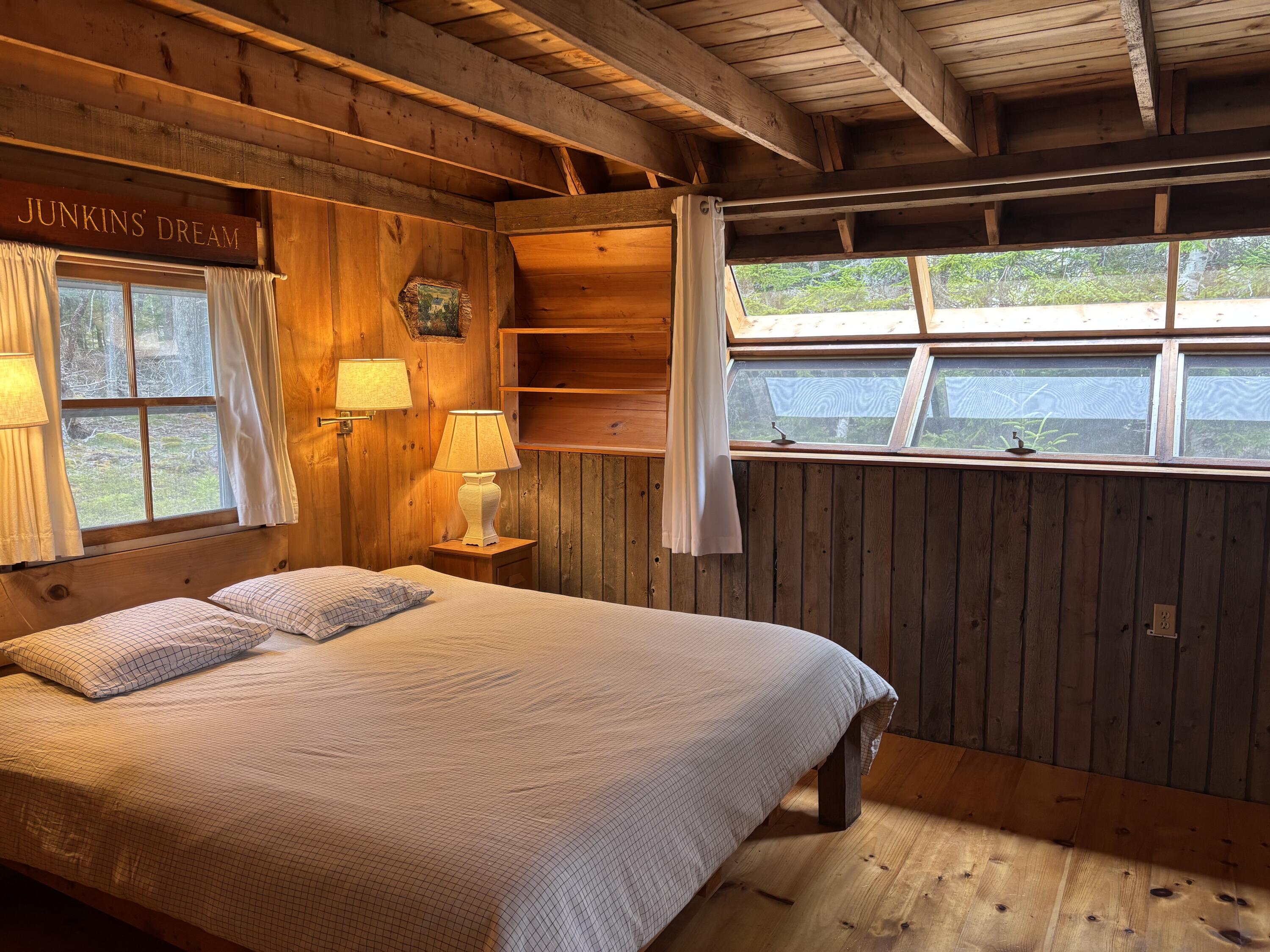 Wood-paneled bedroom with a large bed and long windows overlooking trees.