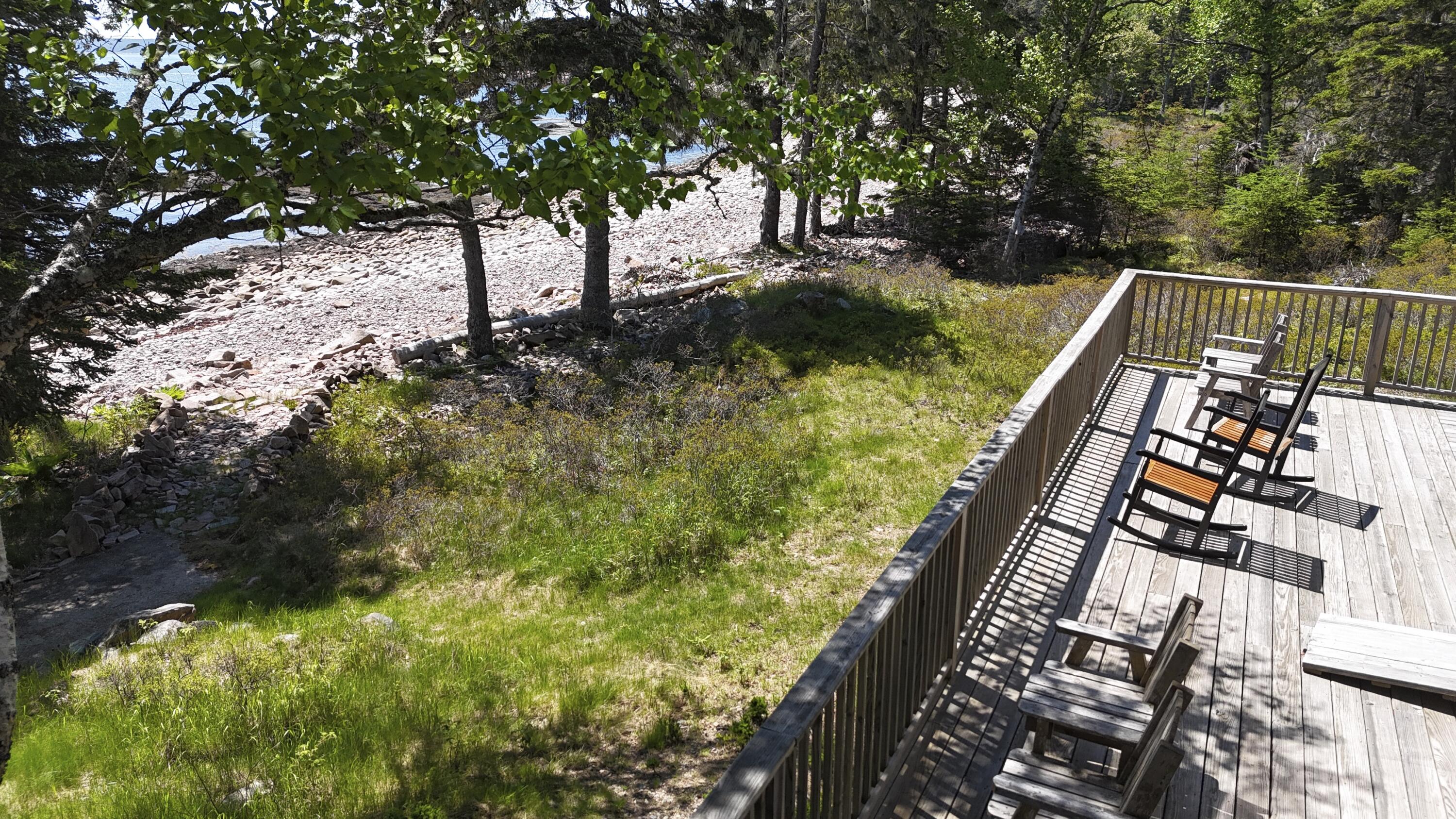 Wooden deck with Adirondack chairs beside a grassy yard and rocky shoreline.