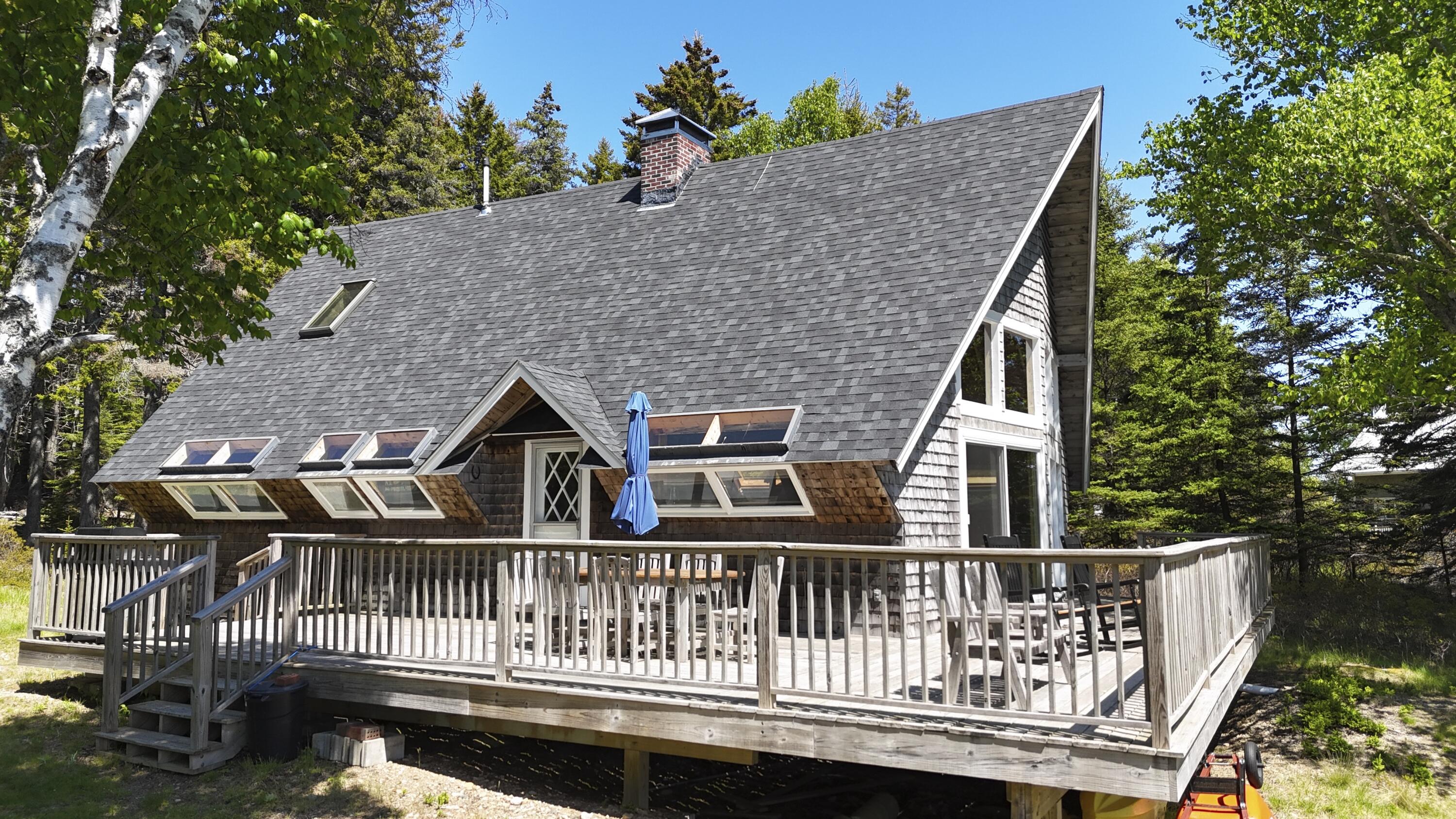 Shingle-sided home with a steep roof and large wraparound deck among trees.