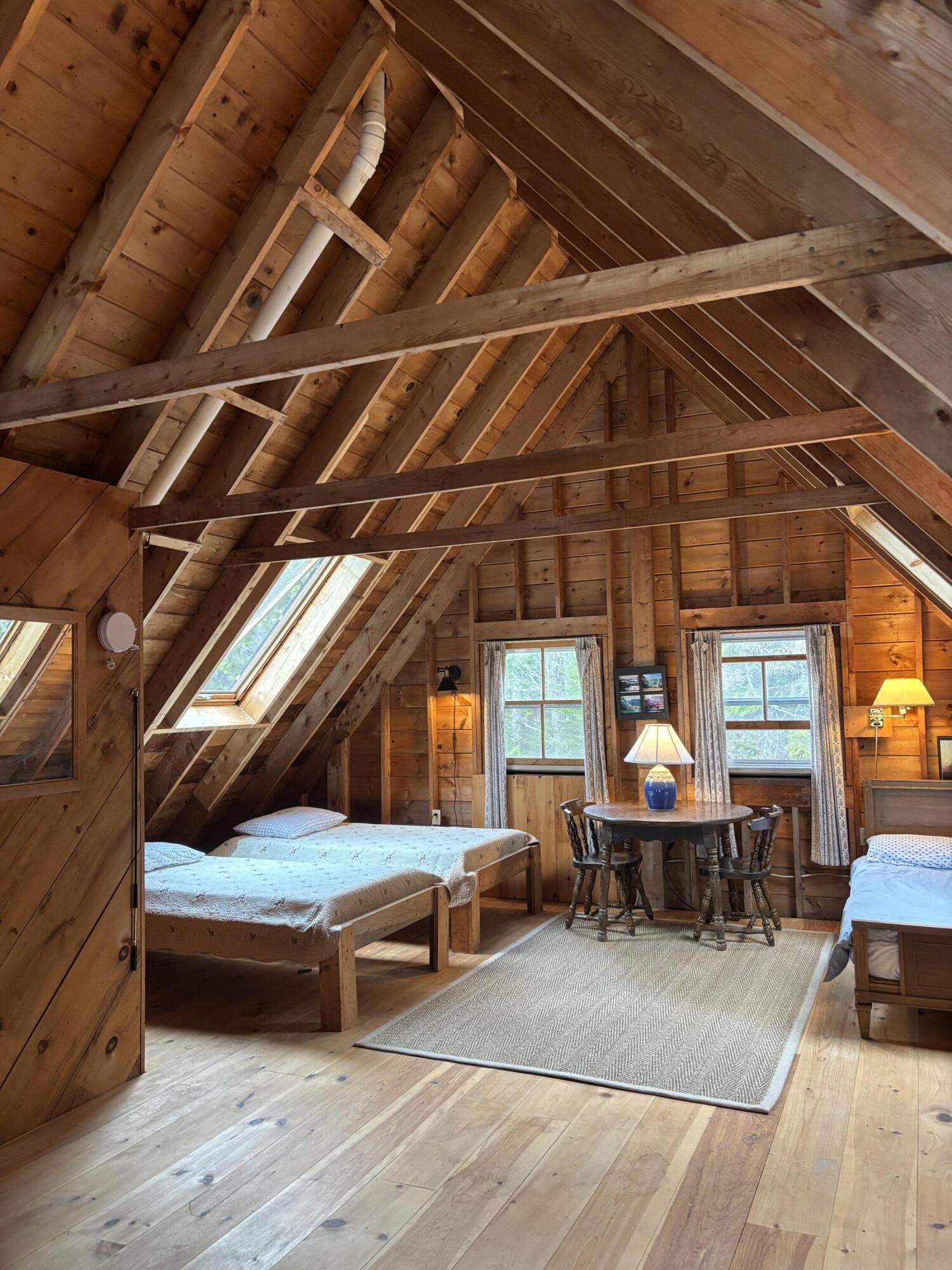 Loft bedroom with exposed timber rafters, skylights, and three beds around a small dining table.