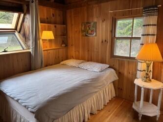 Wood-paneled bedroom with a white bed, skylight, and curtained window.