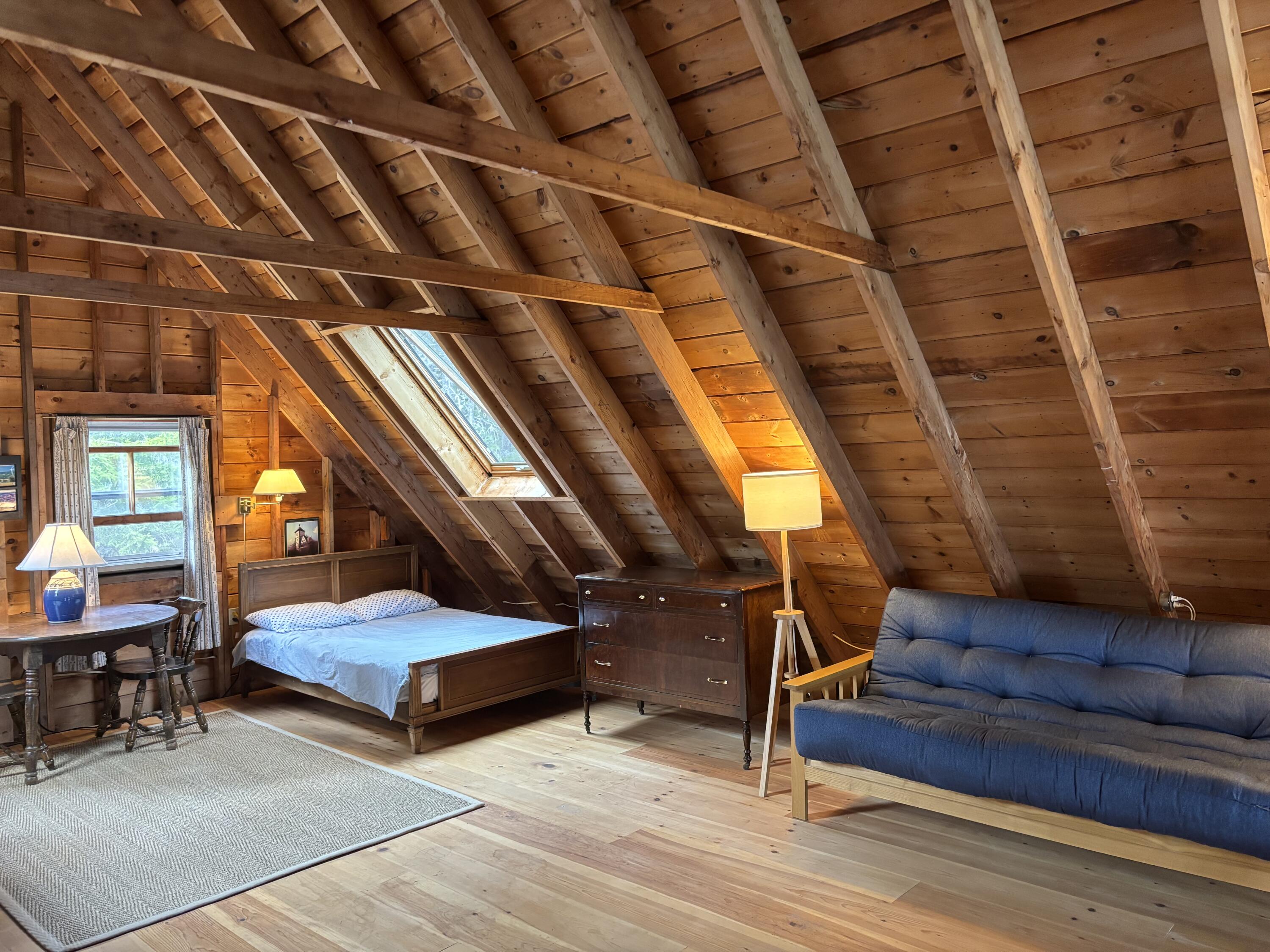 Wood-paneled loft bedroom with exposed rafters, a skylight, a bed, and a blue futon.