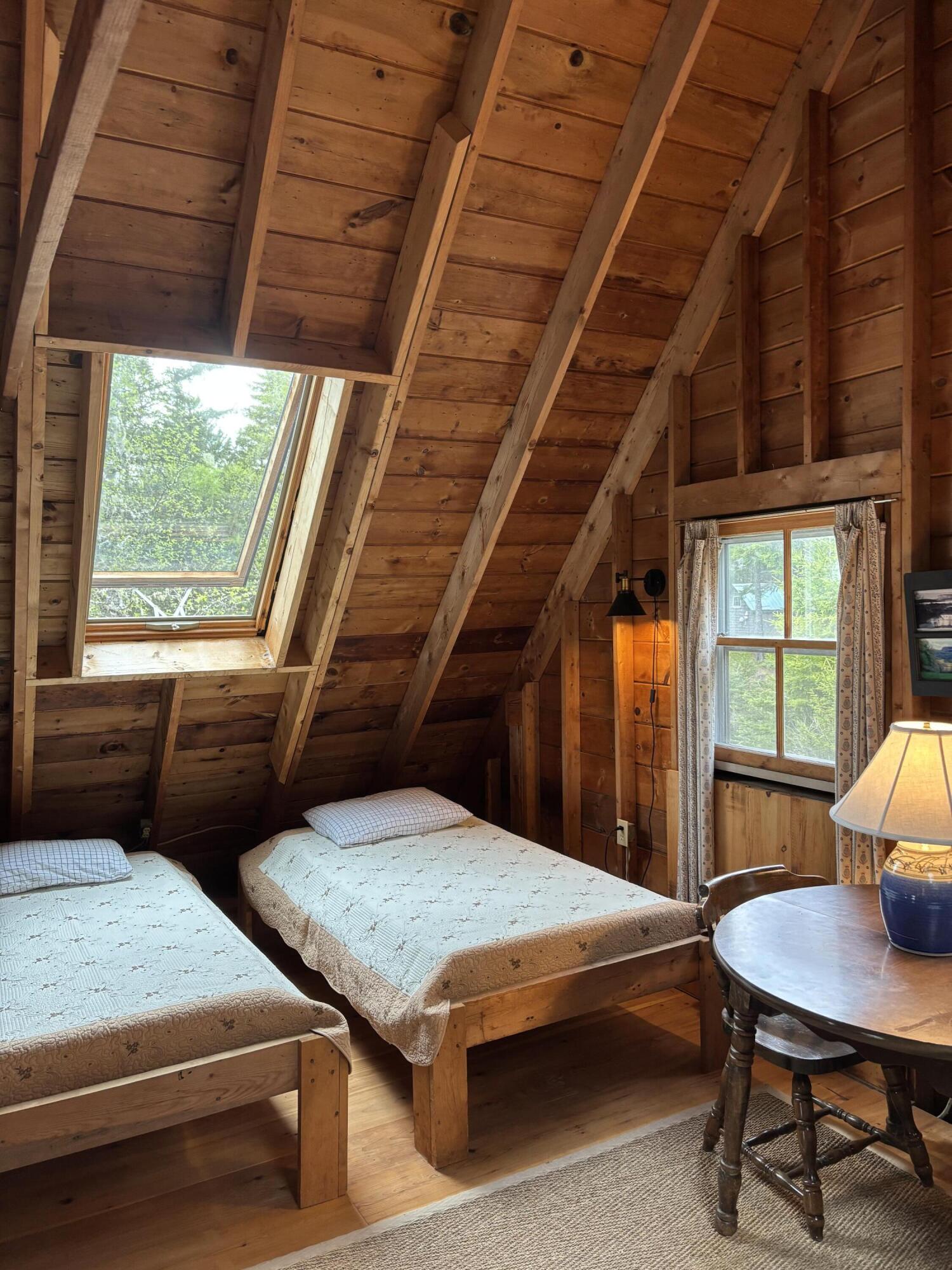 Attic bedroom with two twin beds, exposed timber beams, a large skylight, and a curtained window.