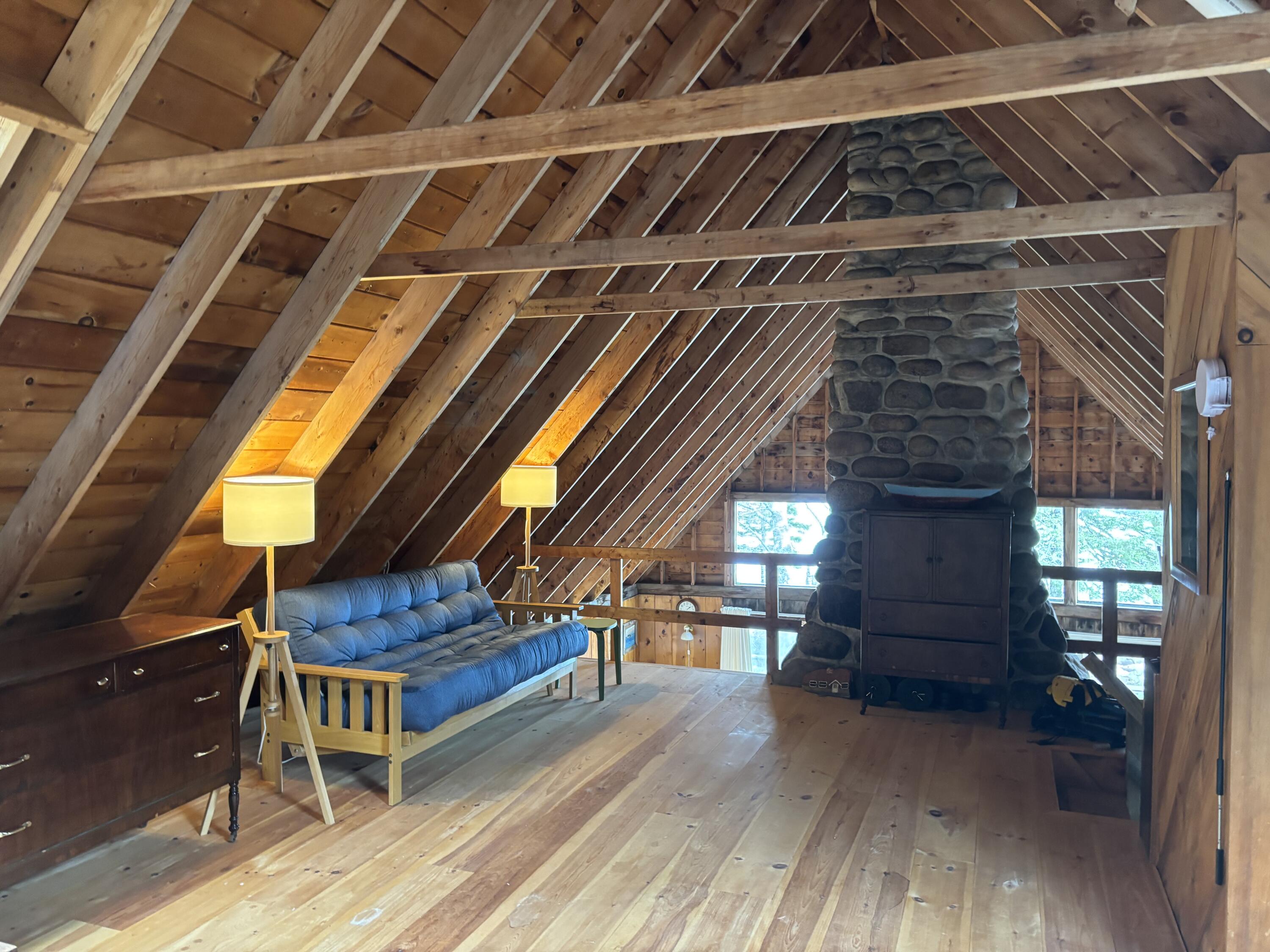 Loft living area with exposed timber rafters, blue sofa, and a large stone fireplace.
