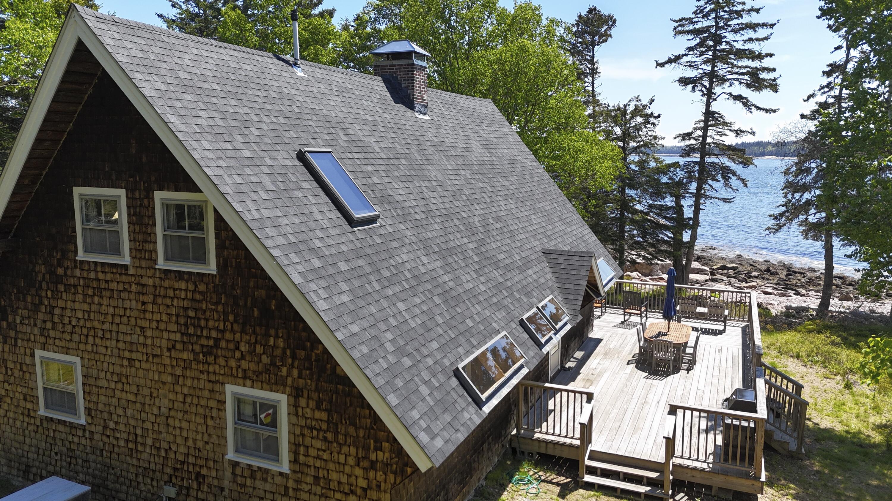 Shingle-sided waterfront house with a large deck overlooking a rocky shoreline.