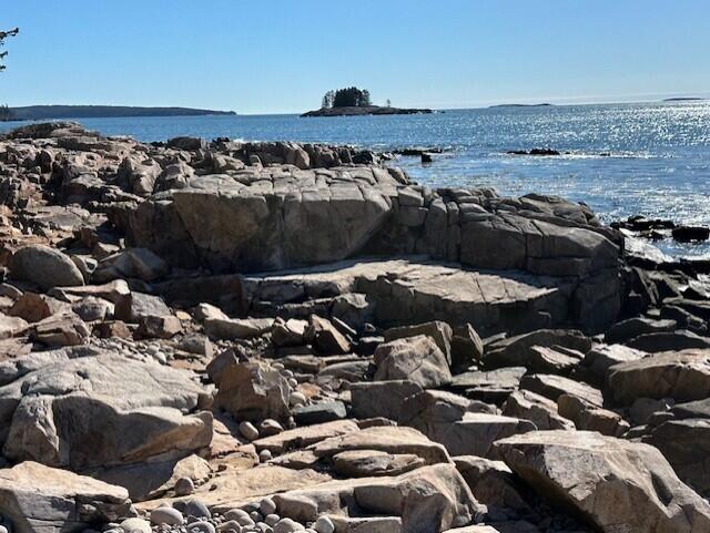 Rocky granite shoreline beside blue ocean, with a small tree-covered island on the horizon.