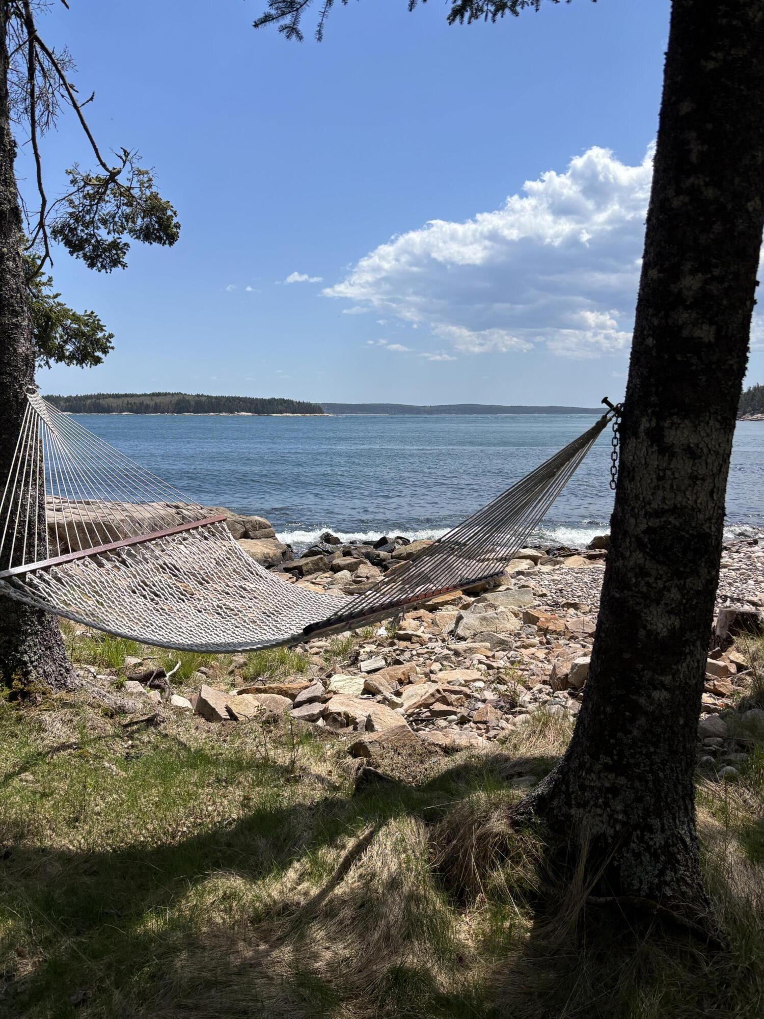 Hammock beside a rocky shoreline overlooking calm ocean water and a forested island.