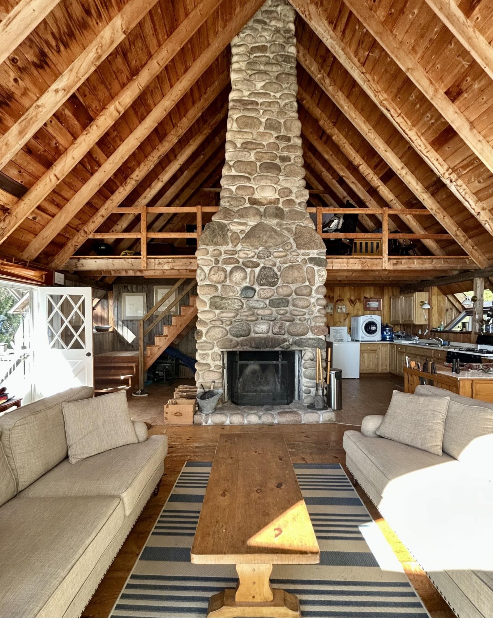 Rustic living room with a towering stone fireplace, exposed timber ceiling, and loft.