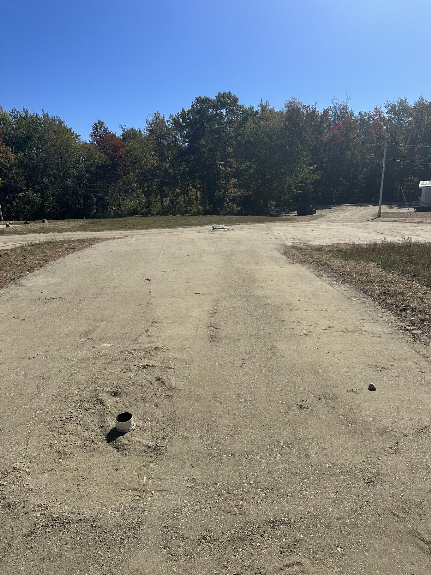 Cleared gravel lot bordered by trees, with a pipe protruding from the ground.