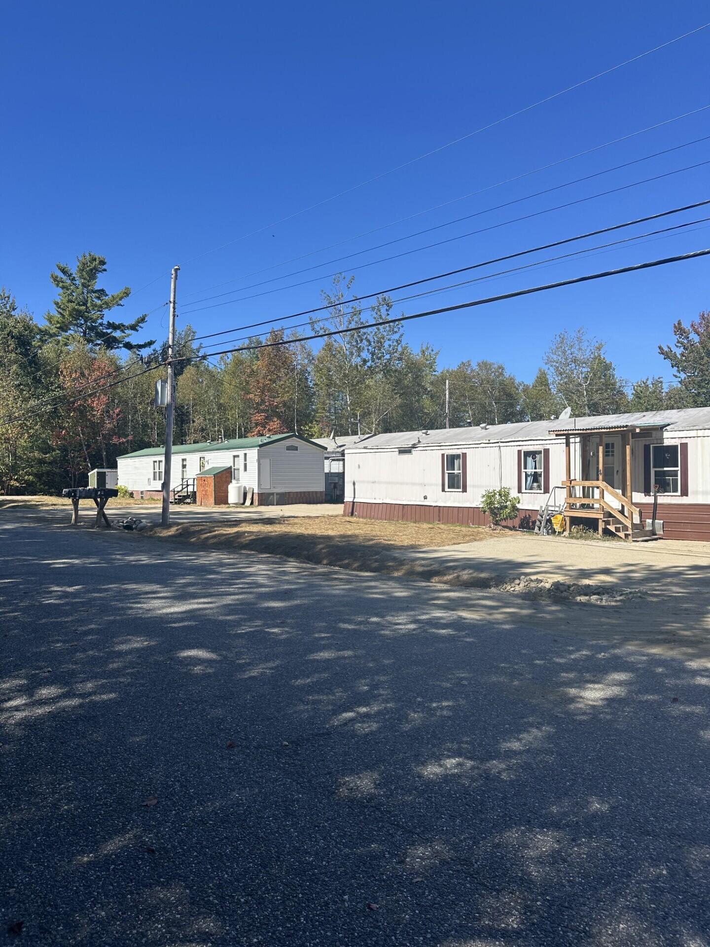 Two manufactured homes beside a gravel driveway, with overhead utility wires and trees behind them.