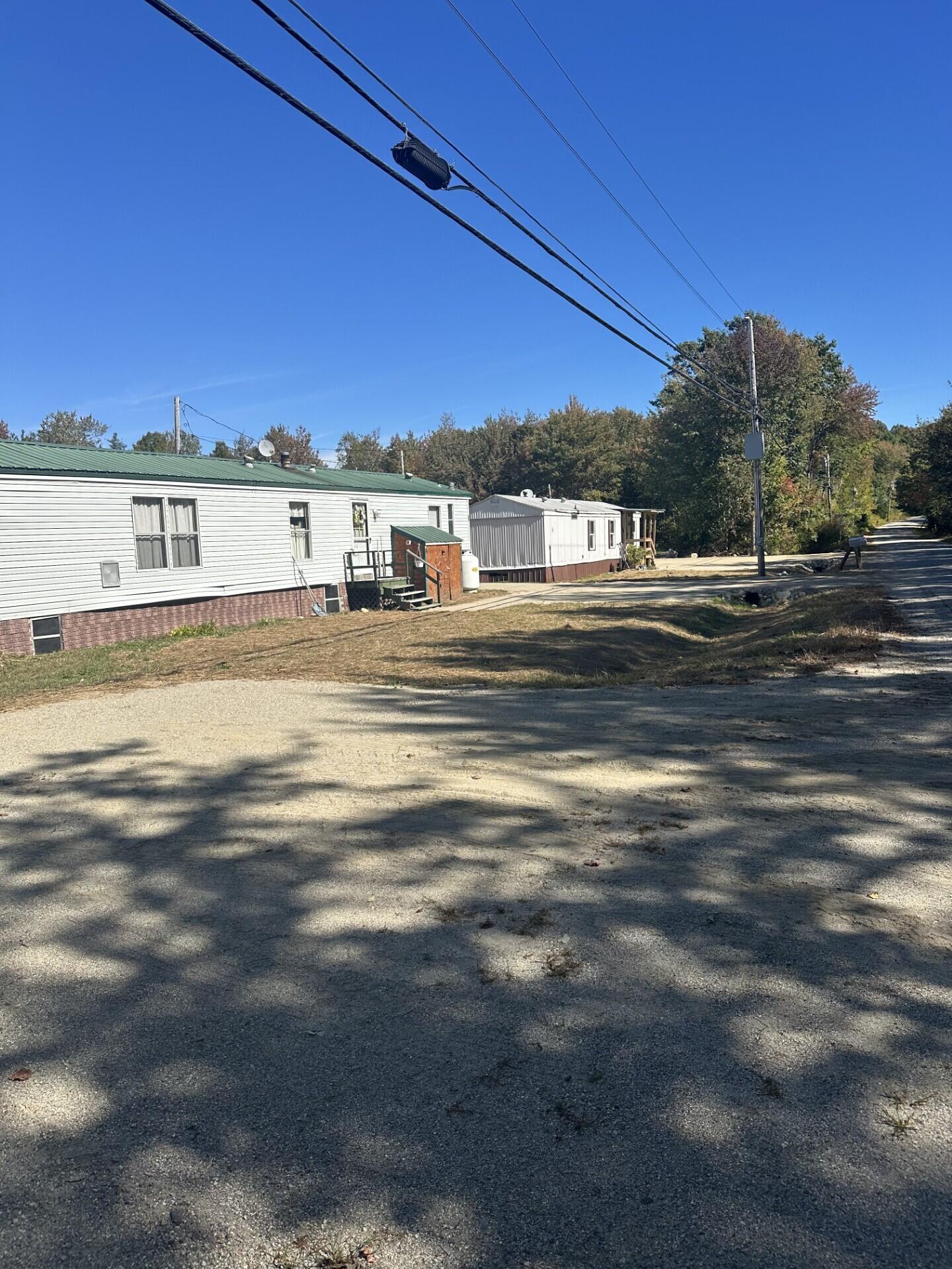 Two manufactured homes beside a gravel drive, with green roofs and overhead utility lines.