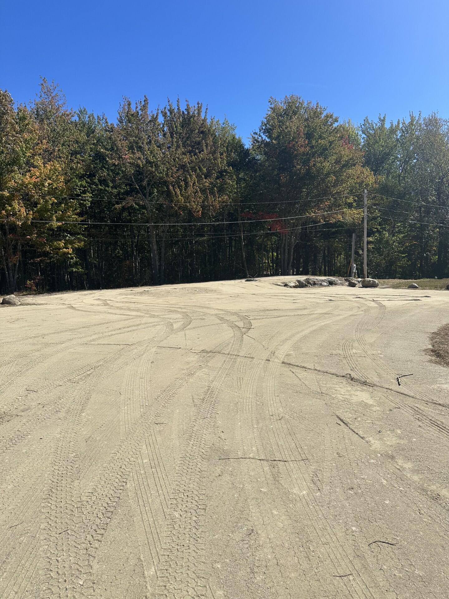 Cleared lot with sandy tire-tracked ground, utility lines, and autumn trees along the edge.