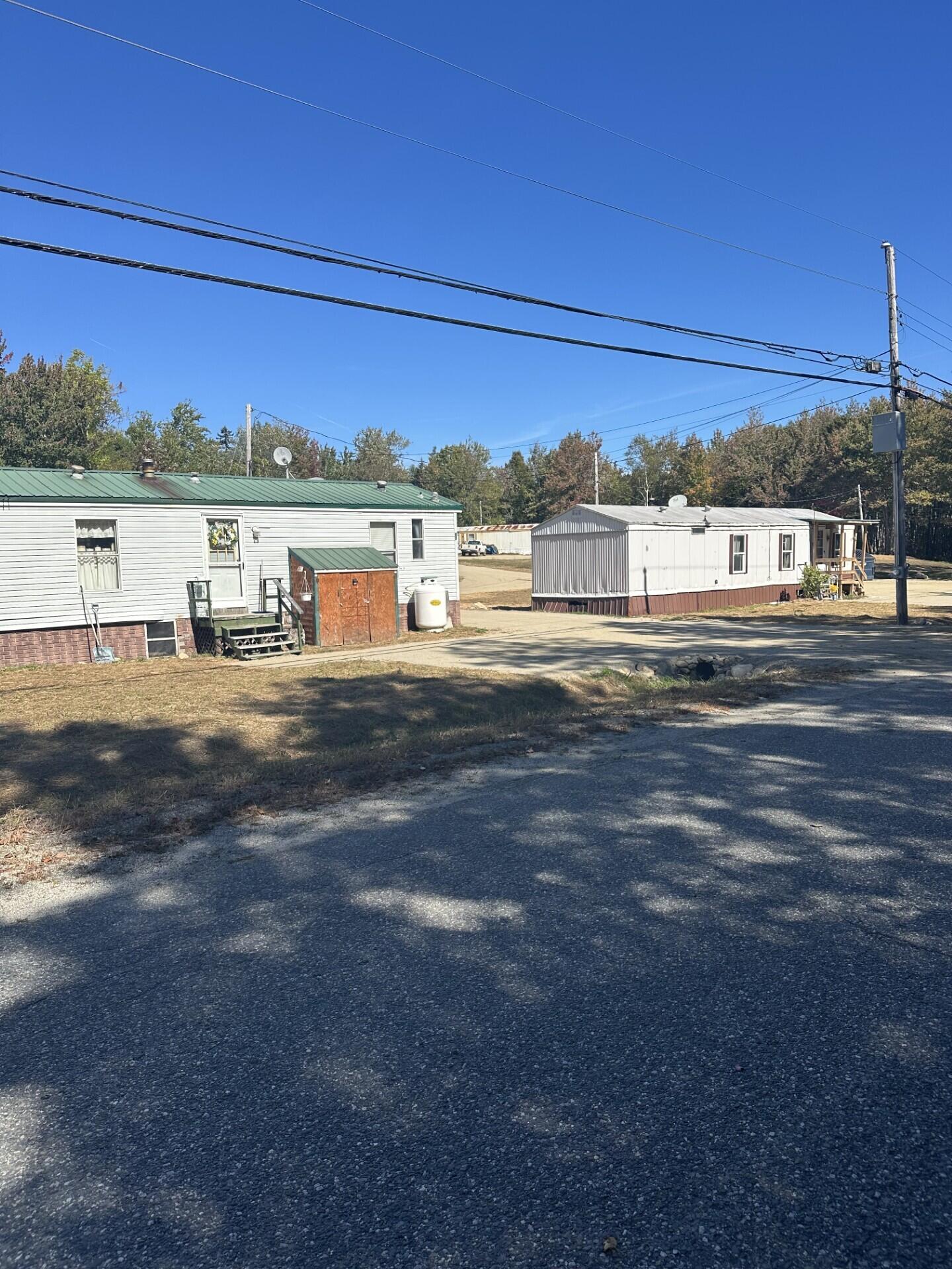 Two manufactured homes beside a paved road, with a green metal roof and overhead utility lines.