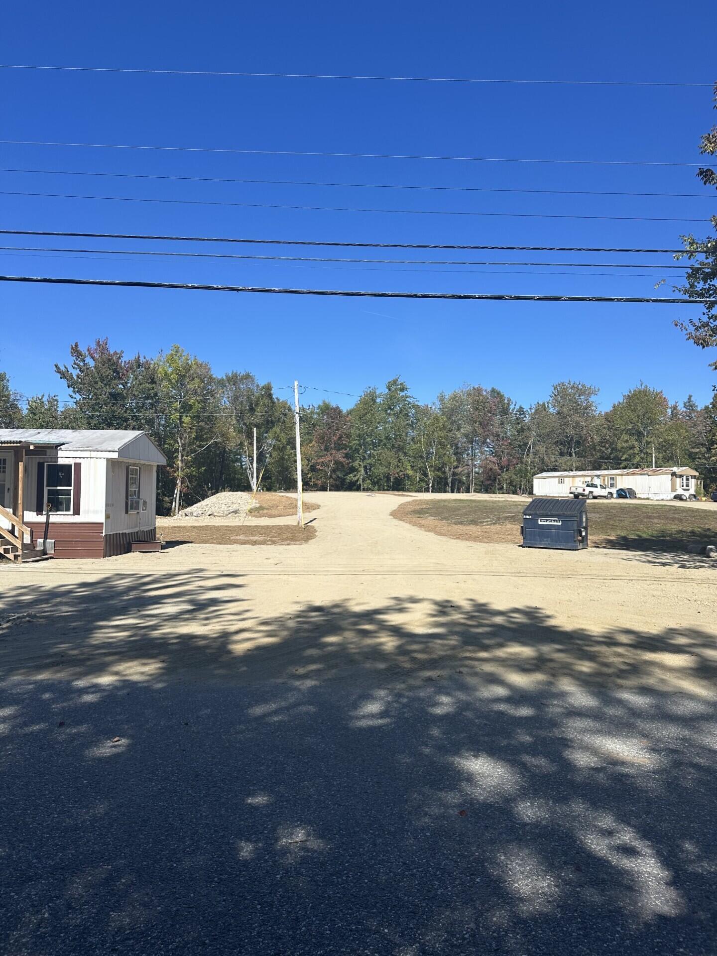 Sandy drive between manufactured homes, with a dumpster and overhead utility wires.