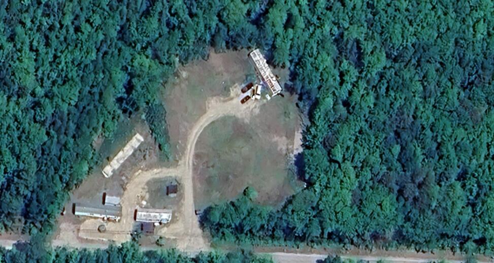 Aerial view of a forested property with a large clearing, dirt drive, and several buildings.