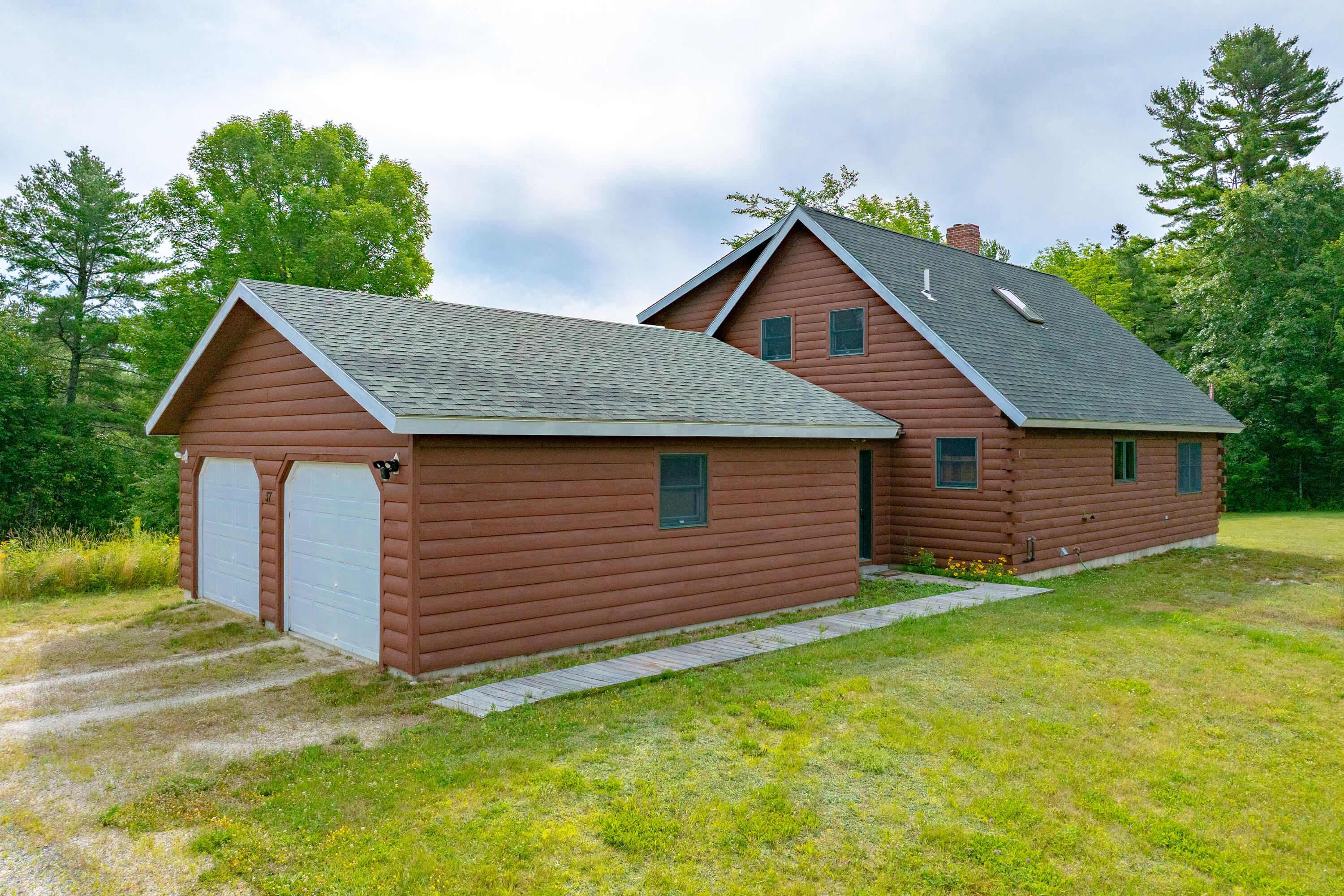 Brown log-sided home with an attached two-car garage, gray roofs, and a wooden walkway across the lawn.