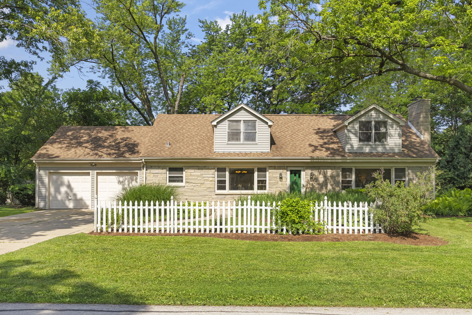 House with a stone facade, double garage, white picket fence, and green front door.