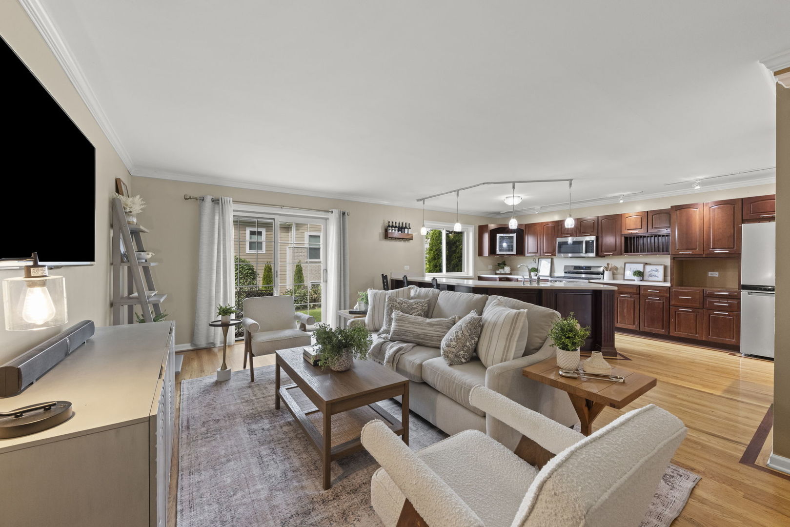 Open-plan living room with a large sectional sofa, sliding glass doors, and dark wood kitchen cabinets.