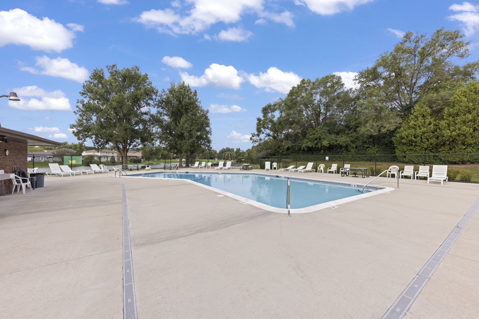 Outdoor swimming pool with a spacious concrete deck and white lounge chairs.