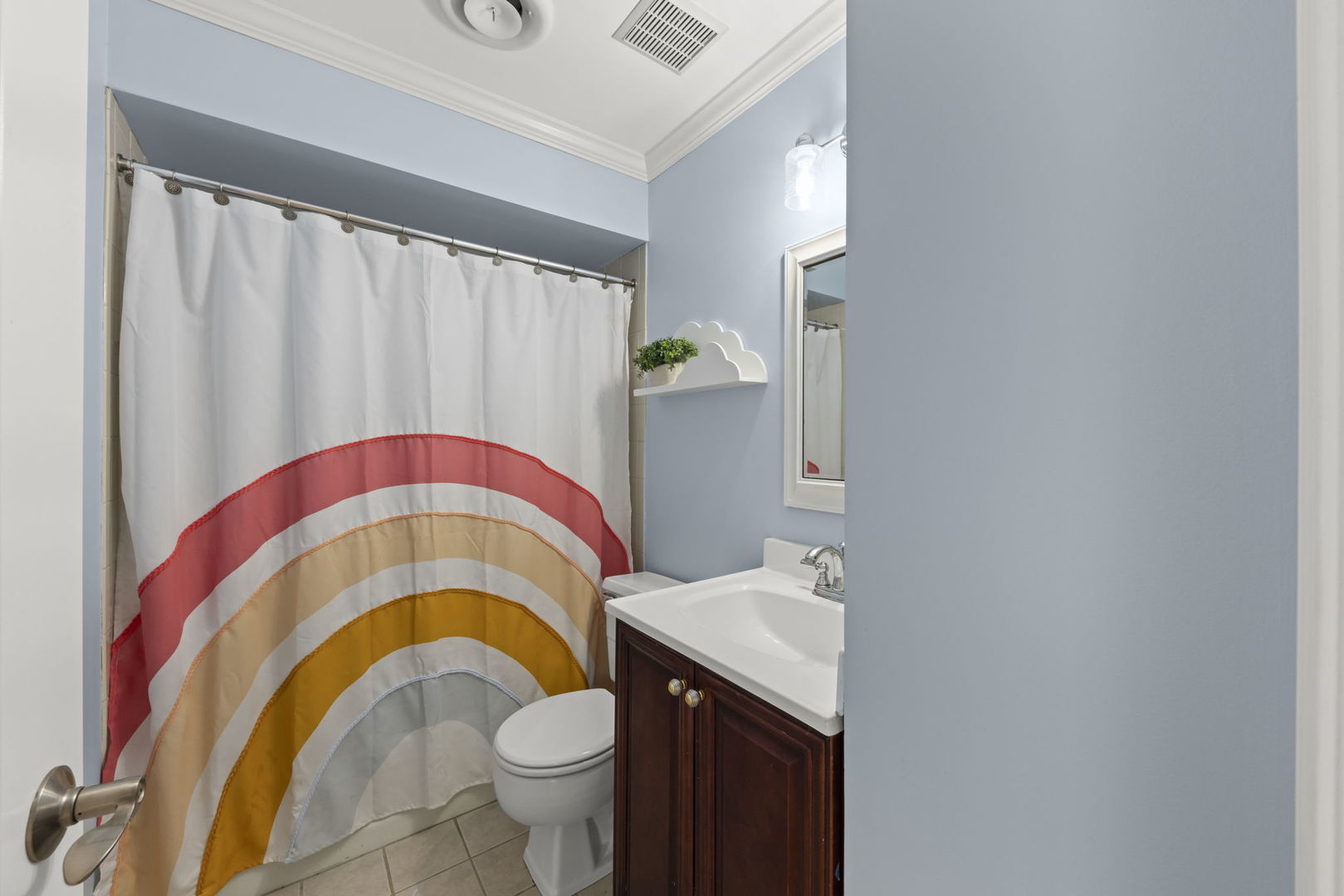 Bathroom with a rainbow-patterned shower curtain, white sink, and dark wood vanity.