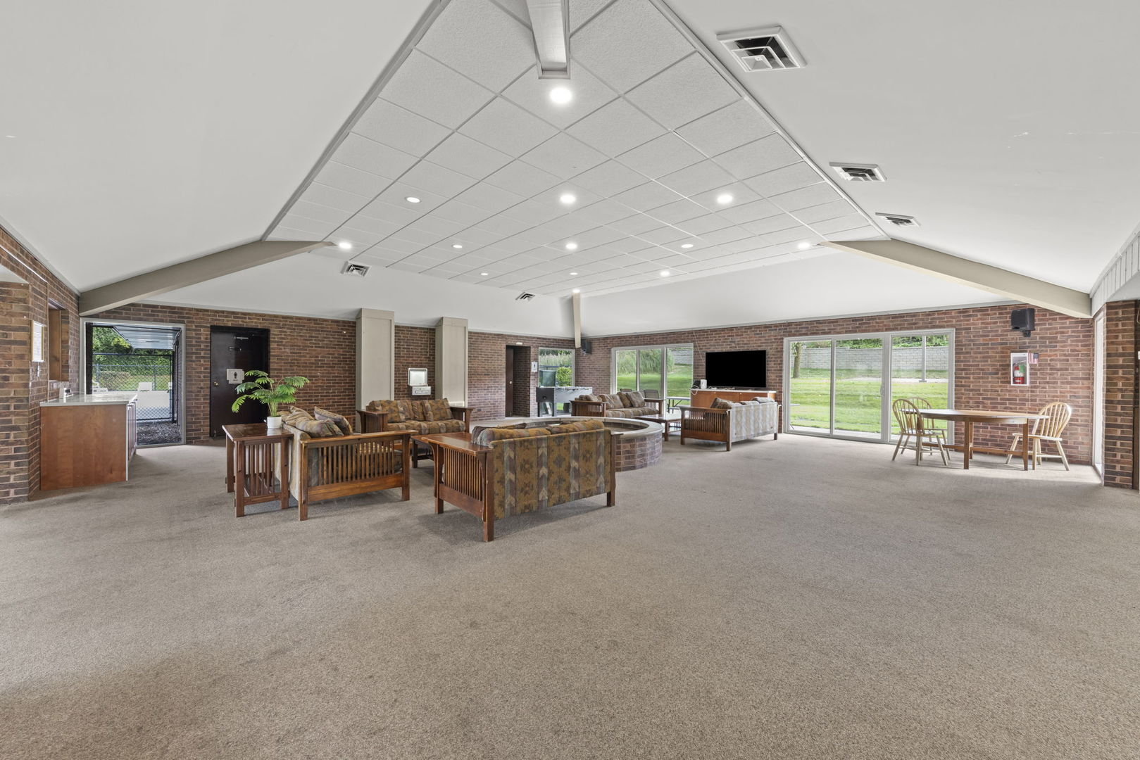 Furnished recreation room with brick walls, vaulted ceiling, and sliding glass doors overlooking a lawn.